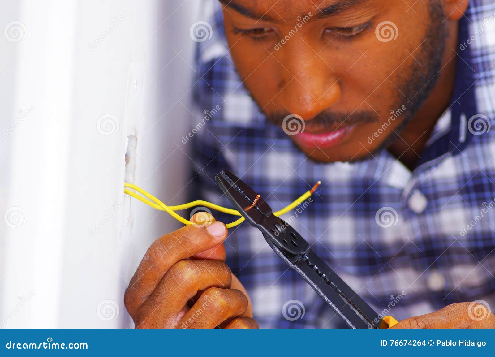 man wearing white and blue shirt working on electrical wall socket wires using screwdriver, electrician concept