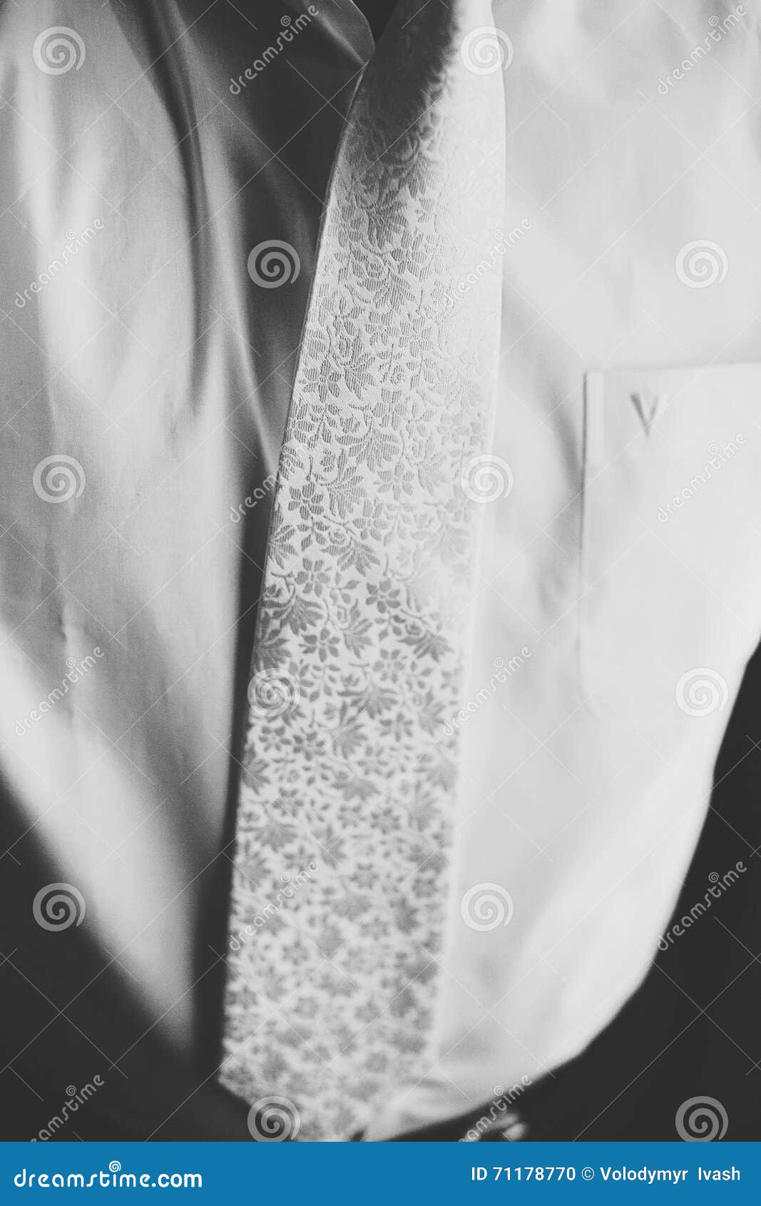 man wears a white tie with a silver fowers over a white shirt