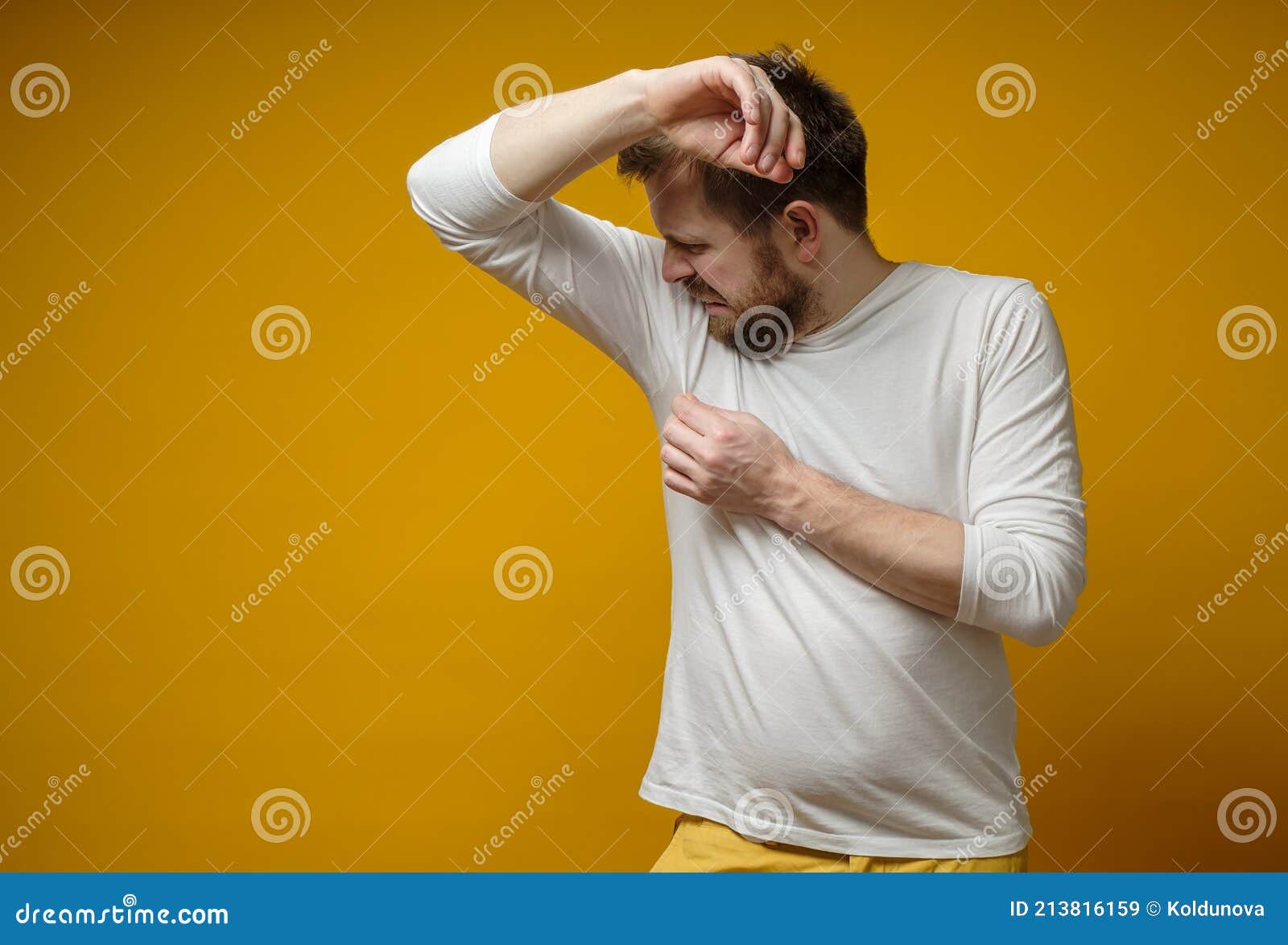 man in a white t-shirt sniffs his armpits, annoyed by the problem of foul perspiration and body stench. copy space.