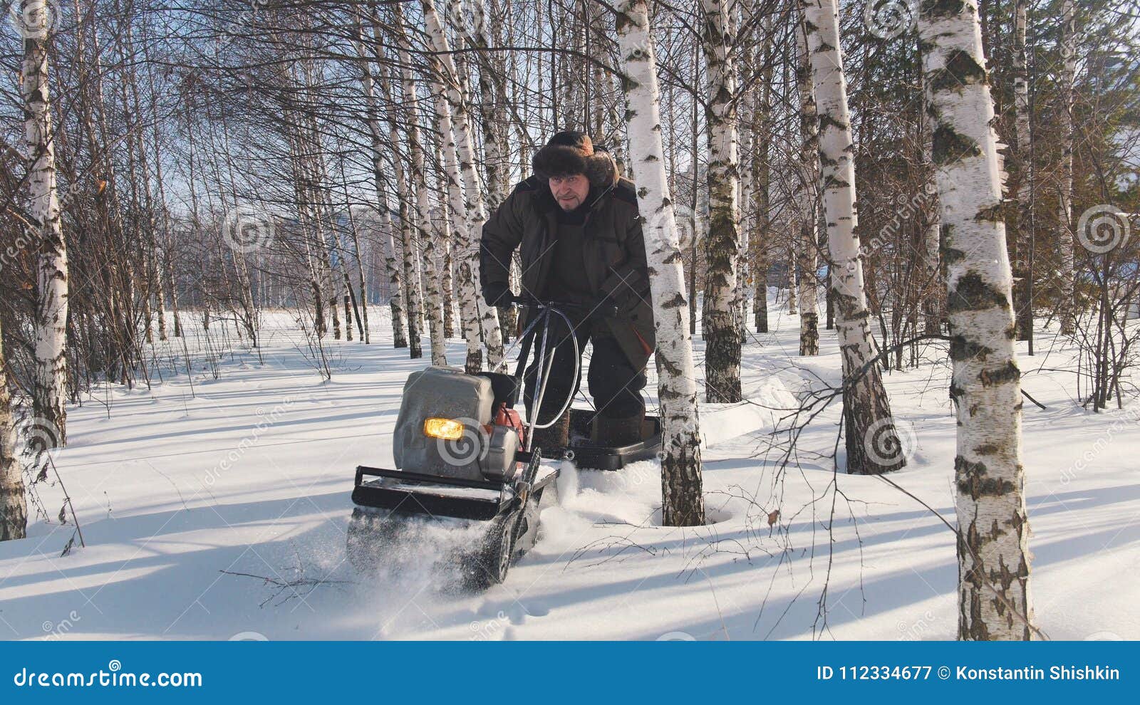 man in winter clothes fast riding on mini snowmobile on deep snowdrifts in the forest and maneuvering between the trees