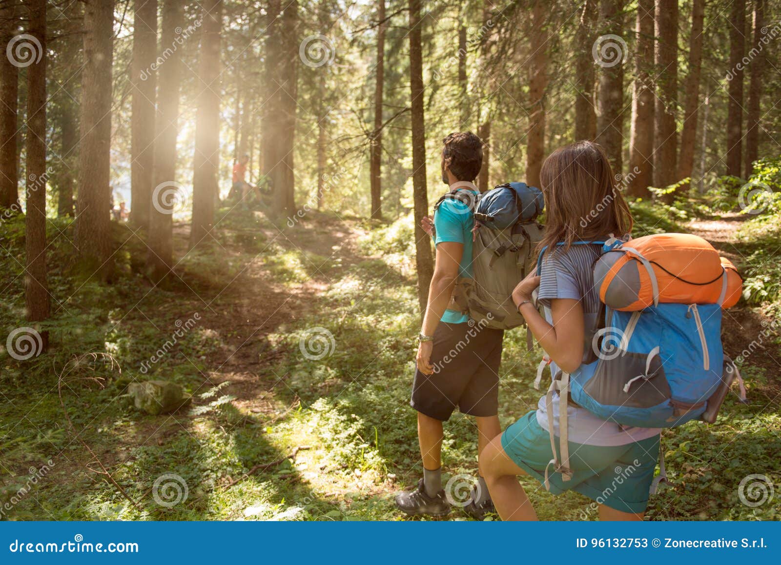 man and woman with backpack walking on hiking trail path in forest woods during sunny day.group of friends people summer