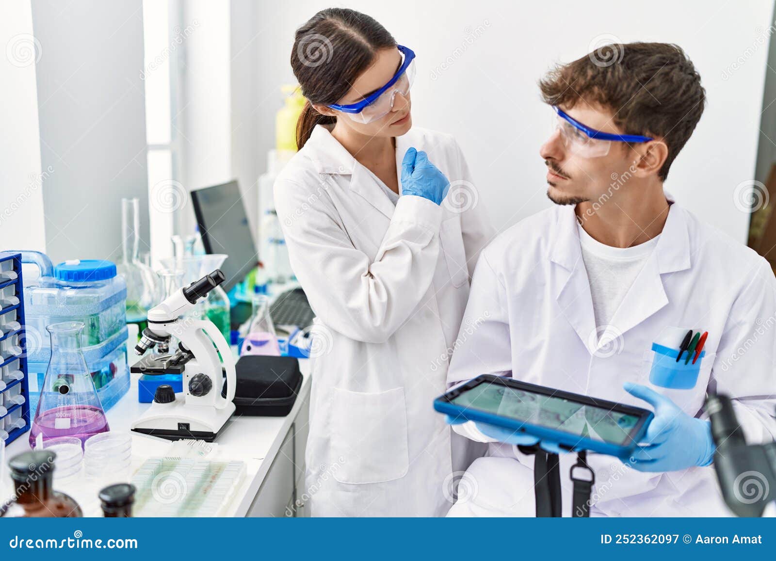 Man and Woman Partners Wearing Scientist Uniform Using Touchpad with