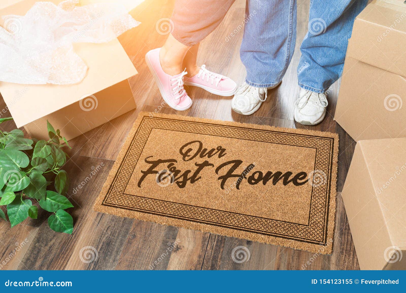 man and woman unpacking near our first home welcome mat, moving boxes and plant