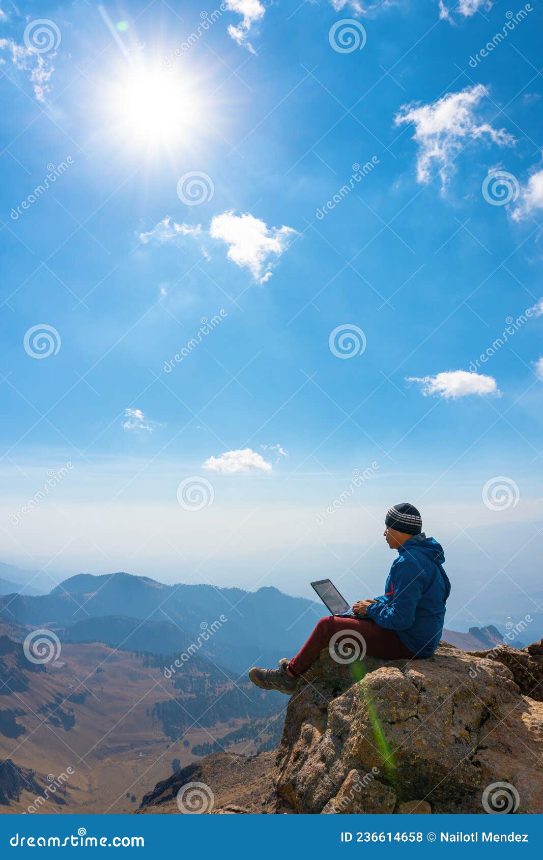 man working on notebook sitting on cliff on top of the mountains