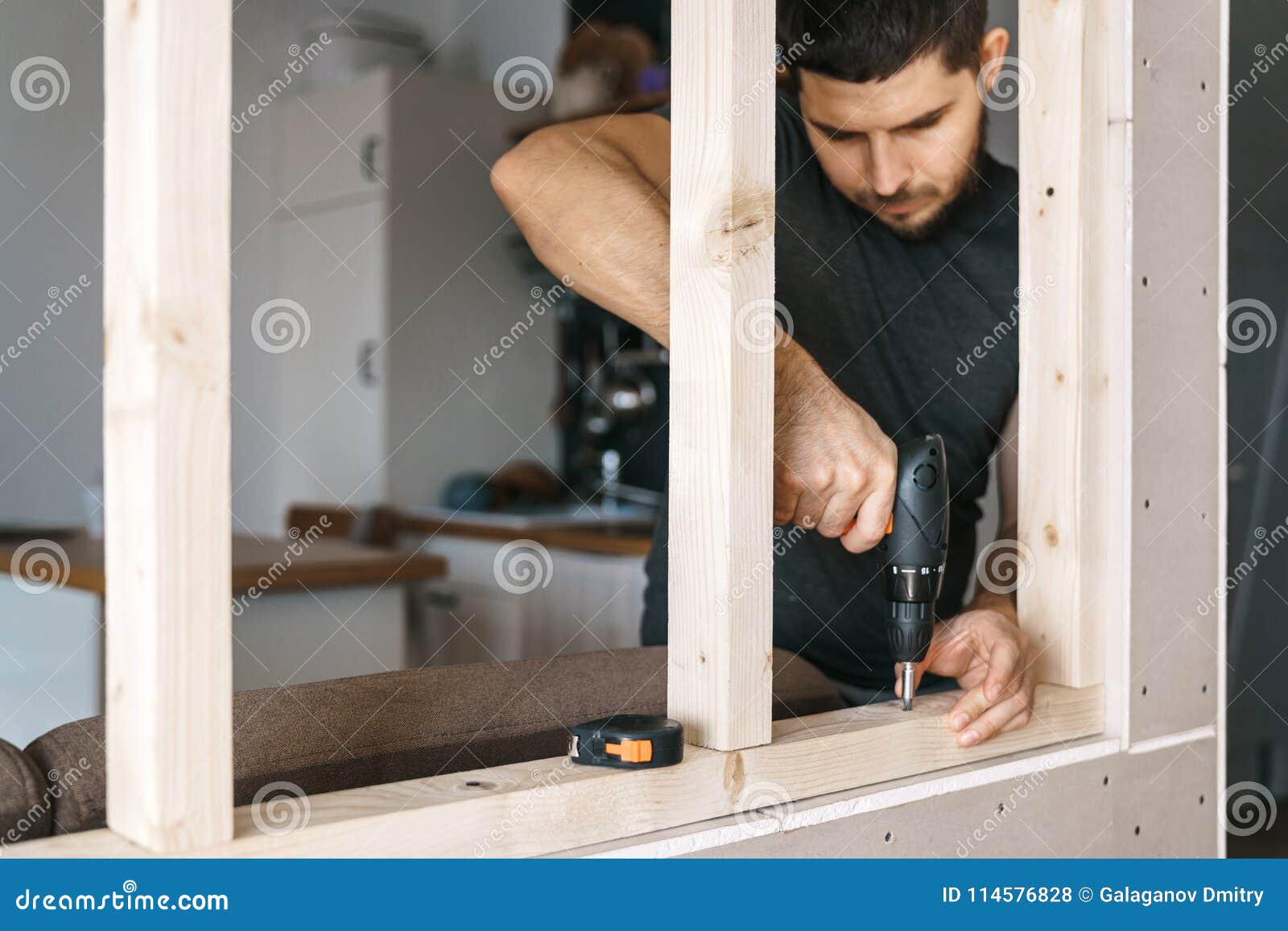 the man works as a screwdriver, fixing a wooden frame for the window to the gypsum plasterboard partition.