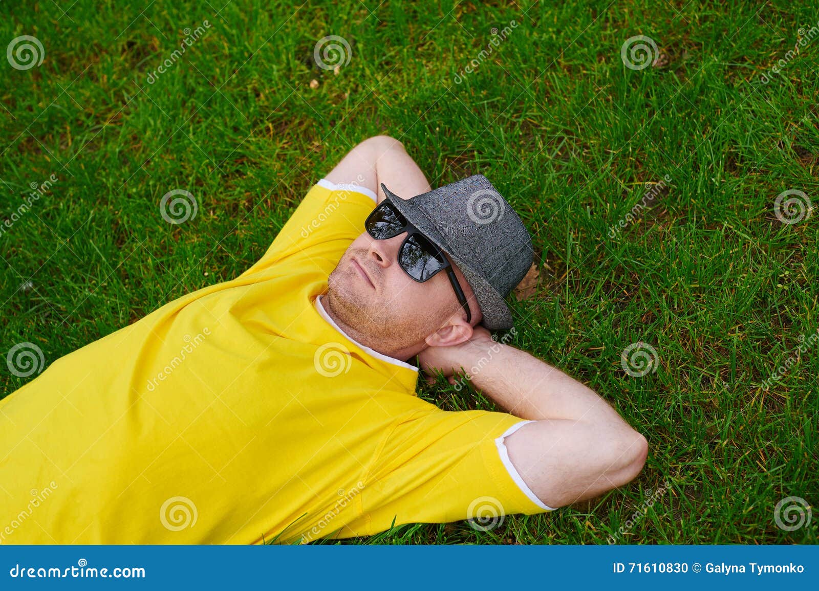Man in a Yellow Tshirt and Hat Lying on the Grass Stock Photo Image