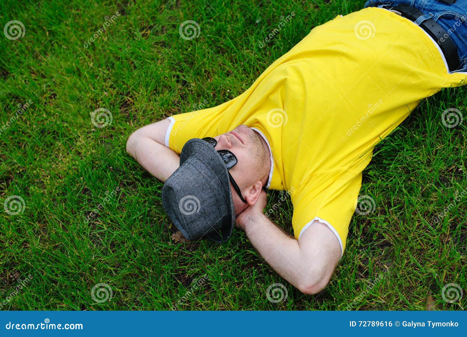 Man in a Yellow Tshirt and Hat Lying on the Grass Stock Photo Image