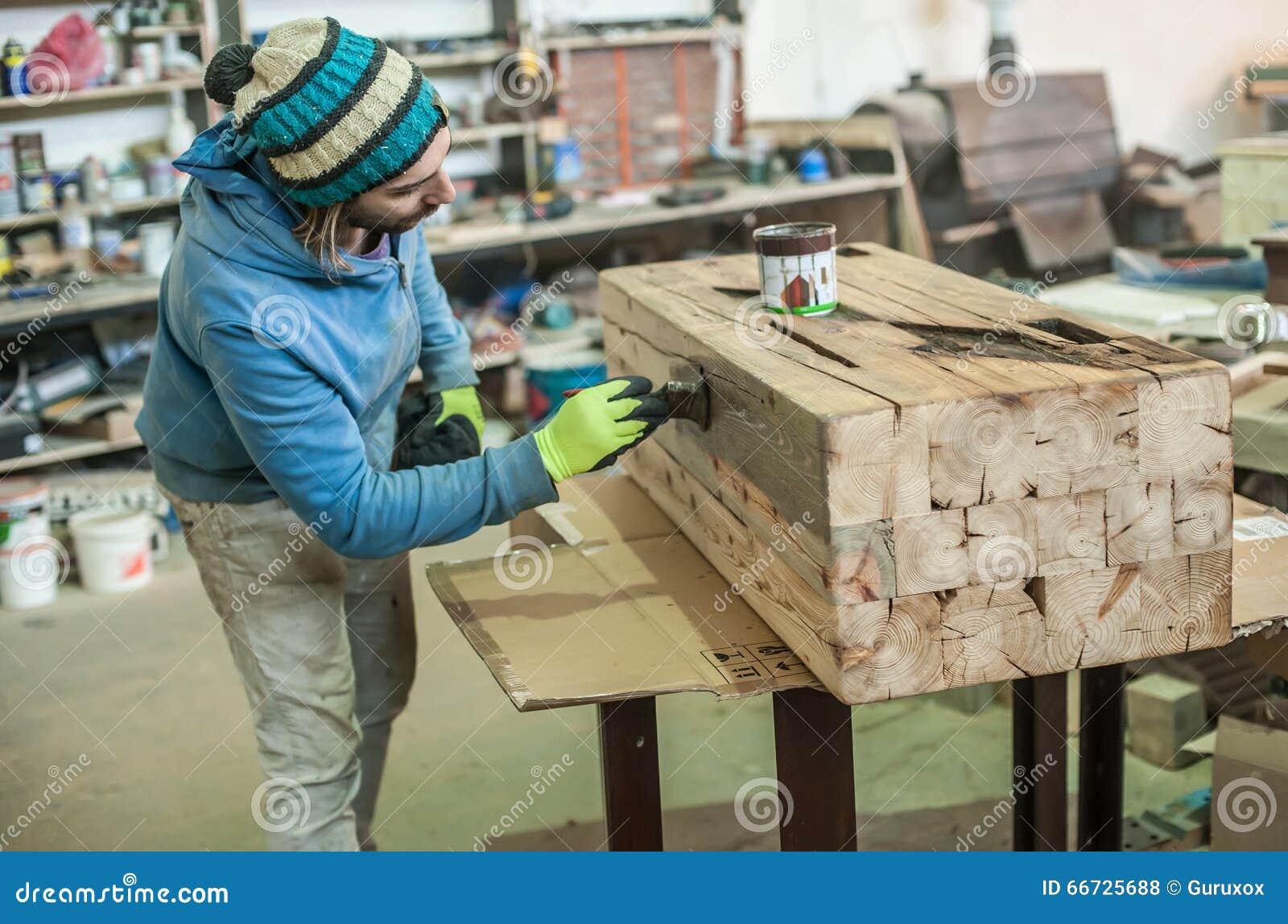 Mancha da escova de pintura
Carpinteiro novo que enverniza uma prateleira de madeira usando o pincel em sua oficina