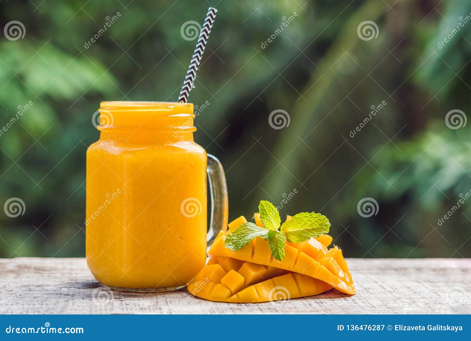 Mango Smoothie in a Glass Mason Jar and Mango on a Green Background