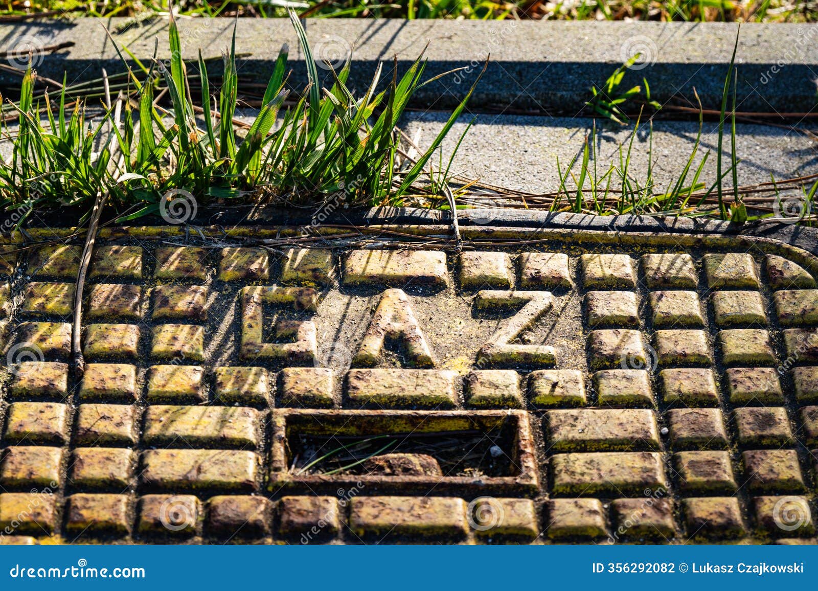 manhole cover with gaz lettering surrounded by grass in a sunny urban setting