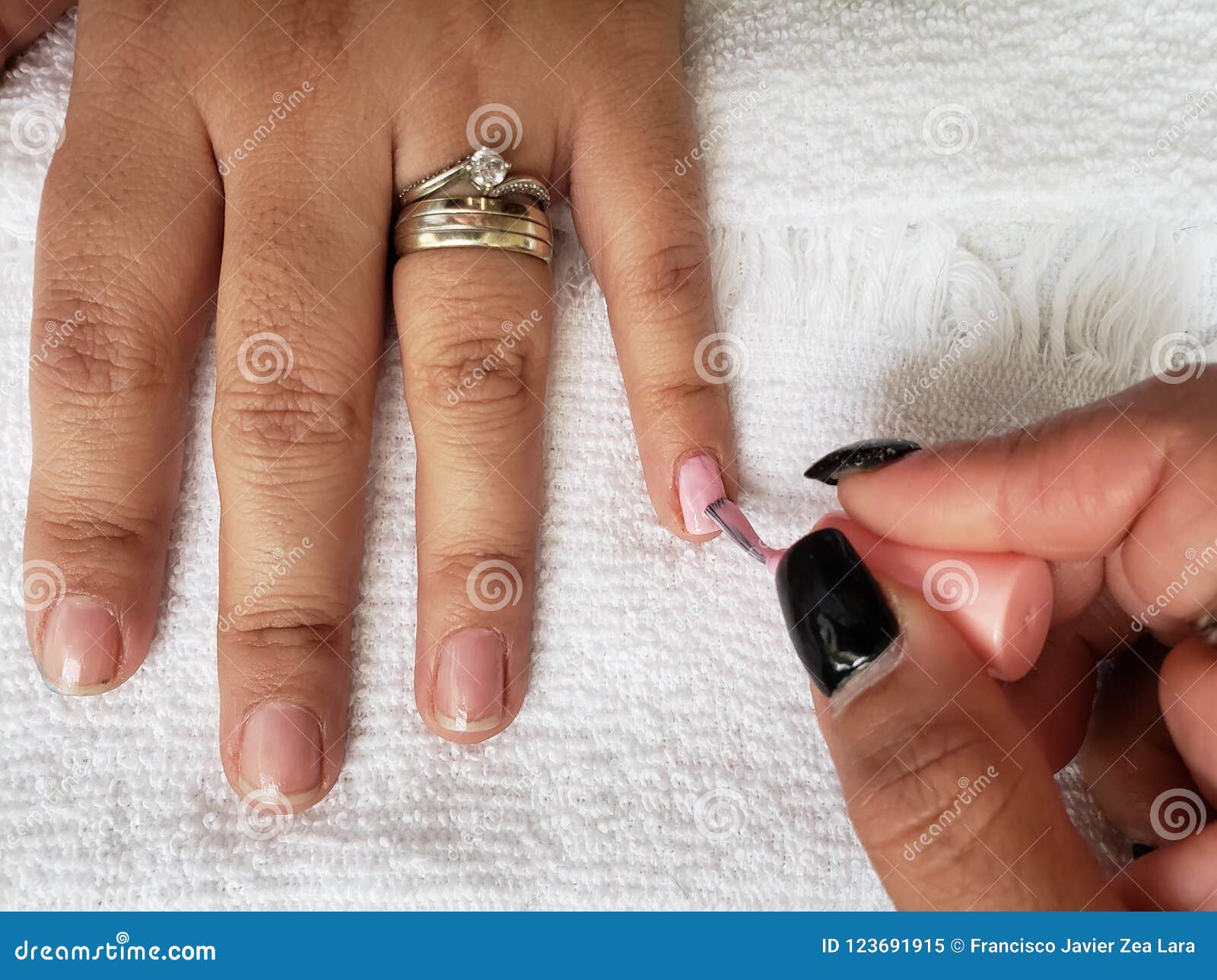 woman painting the fingernails of another woman with light pink nail polish