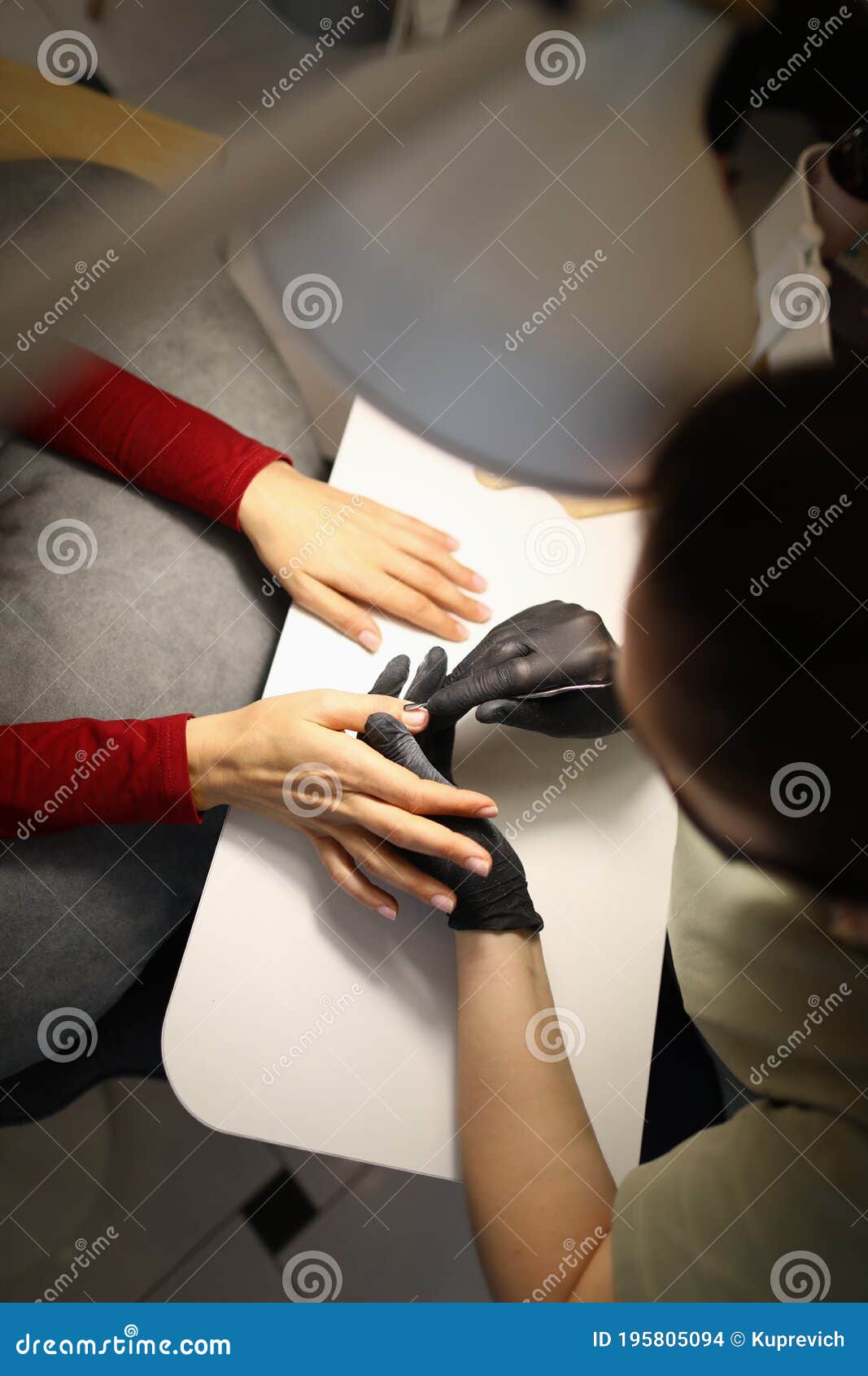 manicurist with gloves treats cuticles on nails in beauty salon.