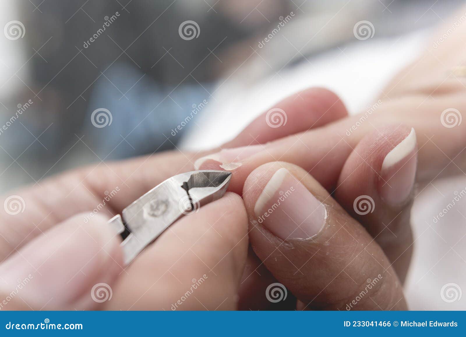 a manicurist uses a pair of nippers to remove a hangnail from the edge of a index fingernail or perionychium.