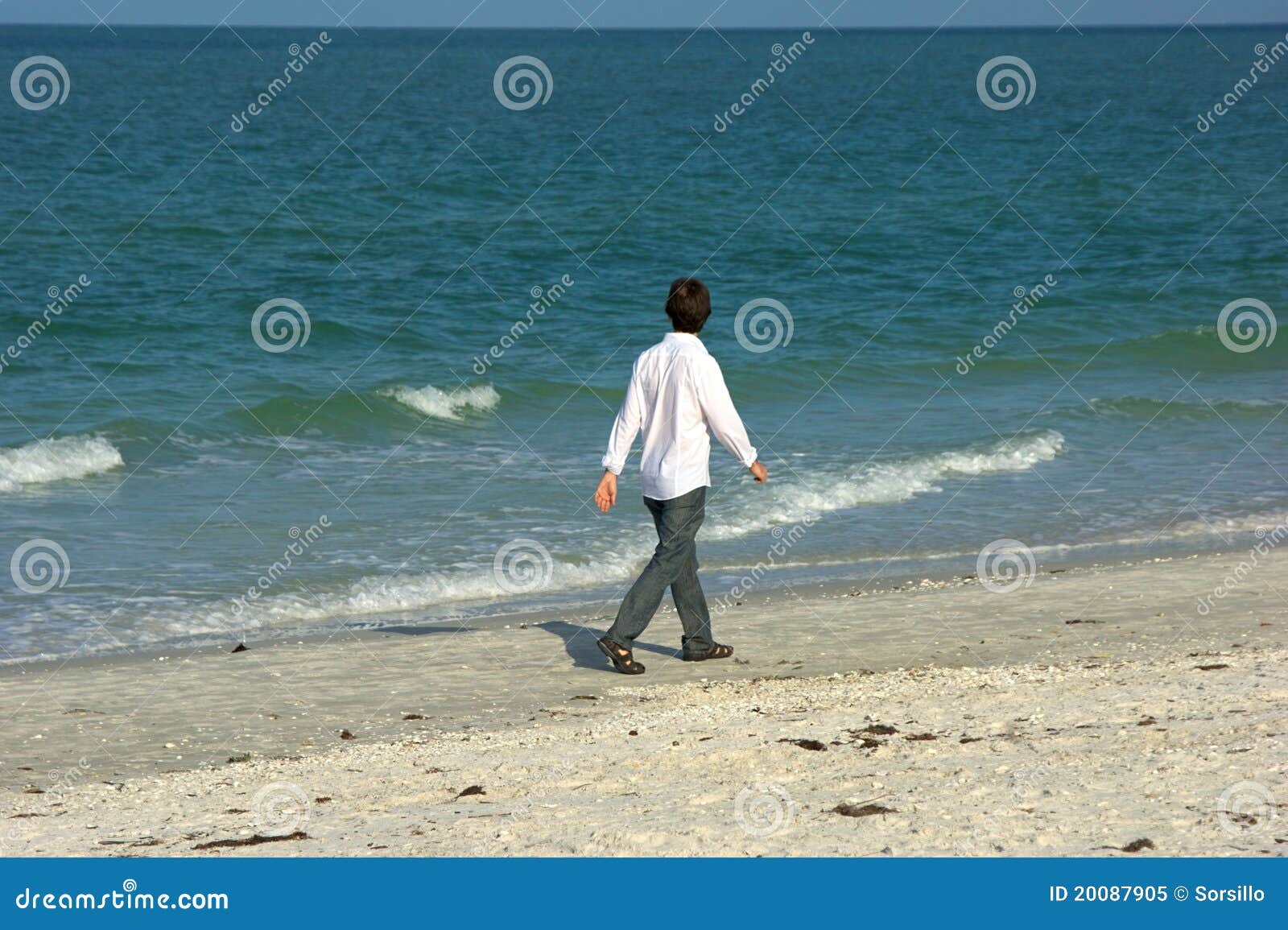 Mann, der entlang den Strand geht. Ein kaukasischer Mann geht draußen entlang den Strand, der heraus den Seetragenden Jeans, den Sandelholzen und einem Smokinghemd auf dem Golf von Mexiko in Florida betrachtet.