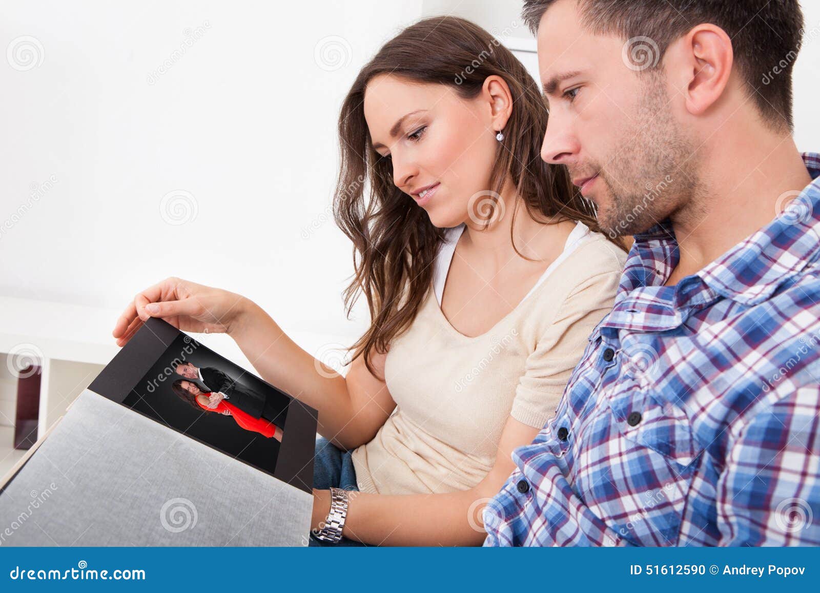 Пригласила вместе с мужем. Мужчина и женщина смотрят фотоальбом. Мужчина рассматривает женщину. Люди рассматривают фотоальбом. Люди рассматривают фотографии.