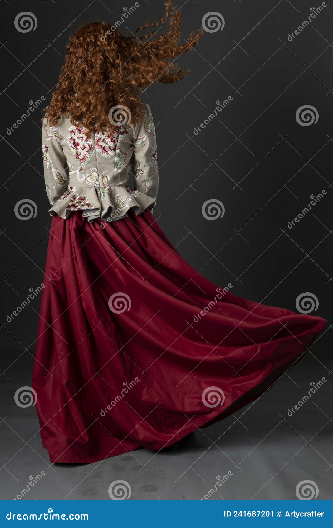 a mannequin with long curly red hair wearing a renaissance-style bodice and red skirt against a studio backdrop
