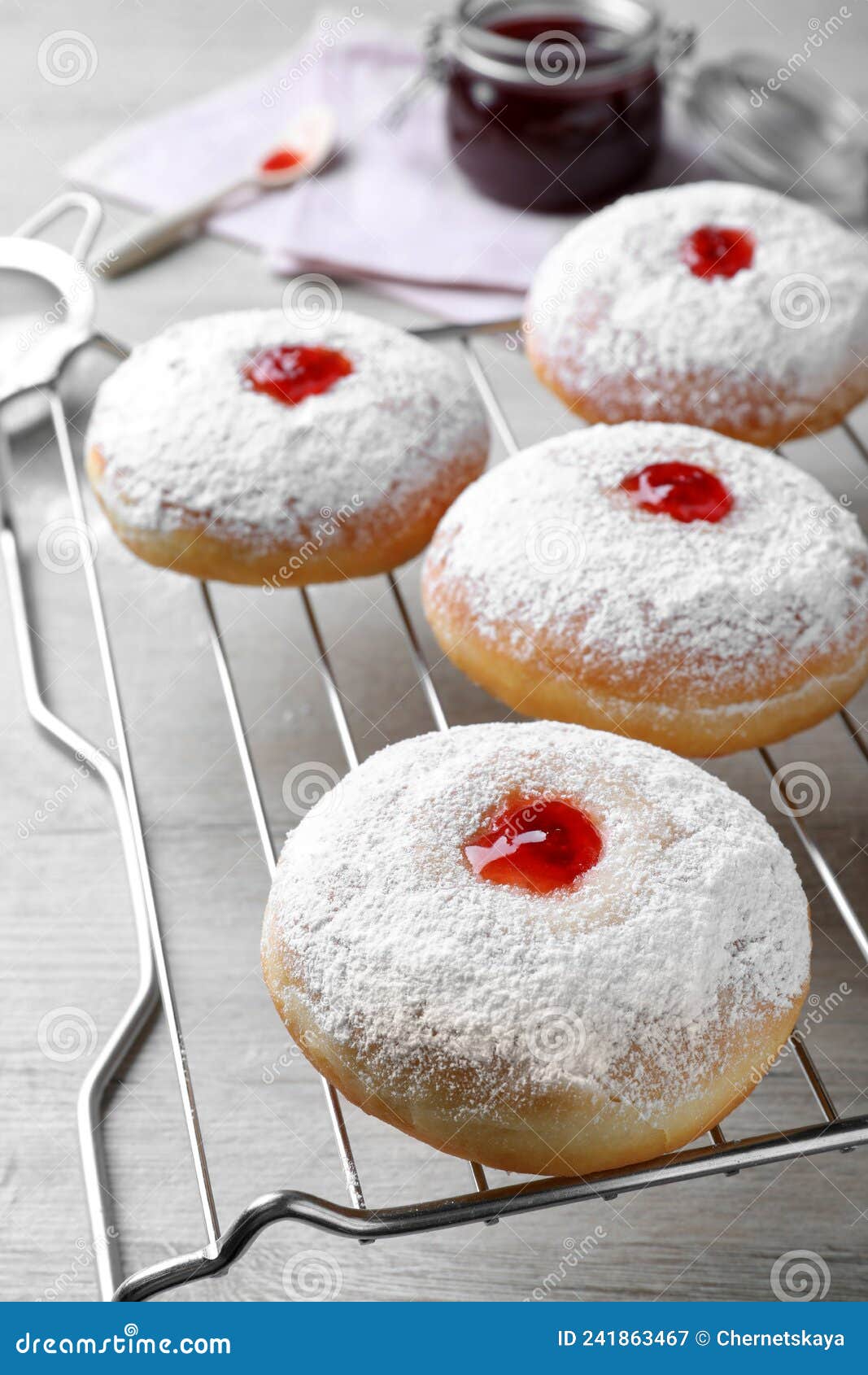 Many Delicious Donuts with Jelly and Powdered Sugar on Cooling Rack