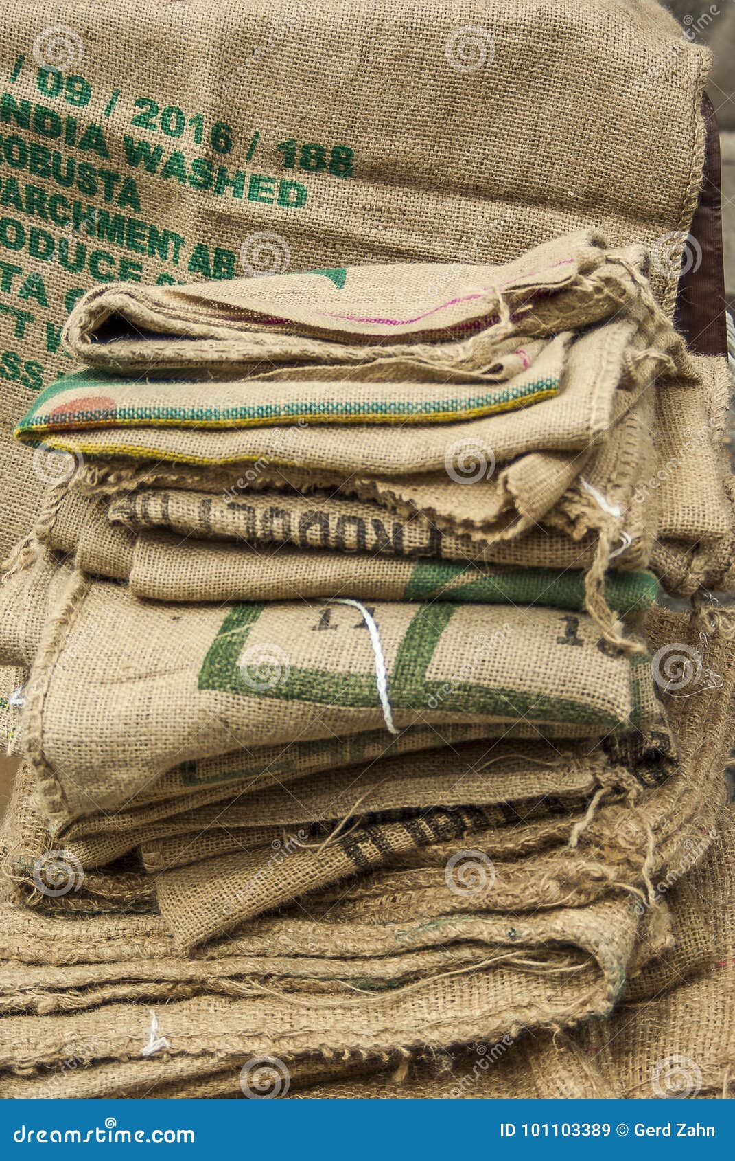 many empty coffee beans bags folded and lying on a pile a sack hangs in the background with non-saying partial print