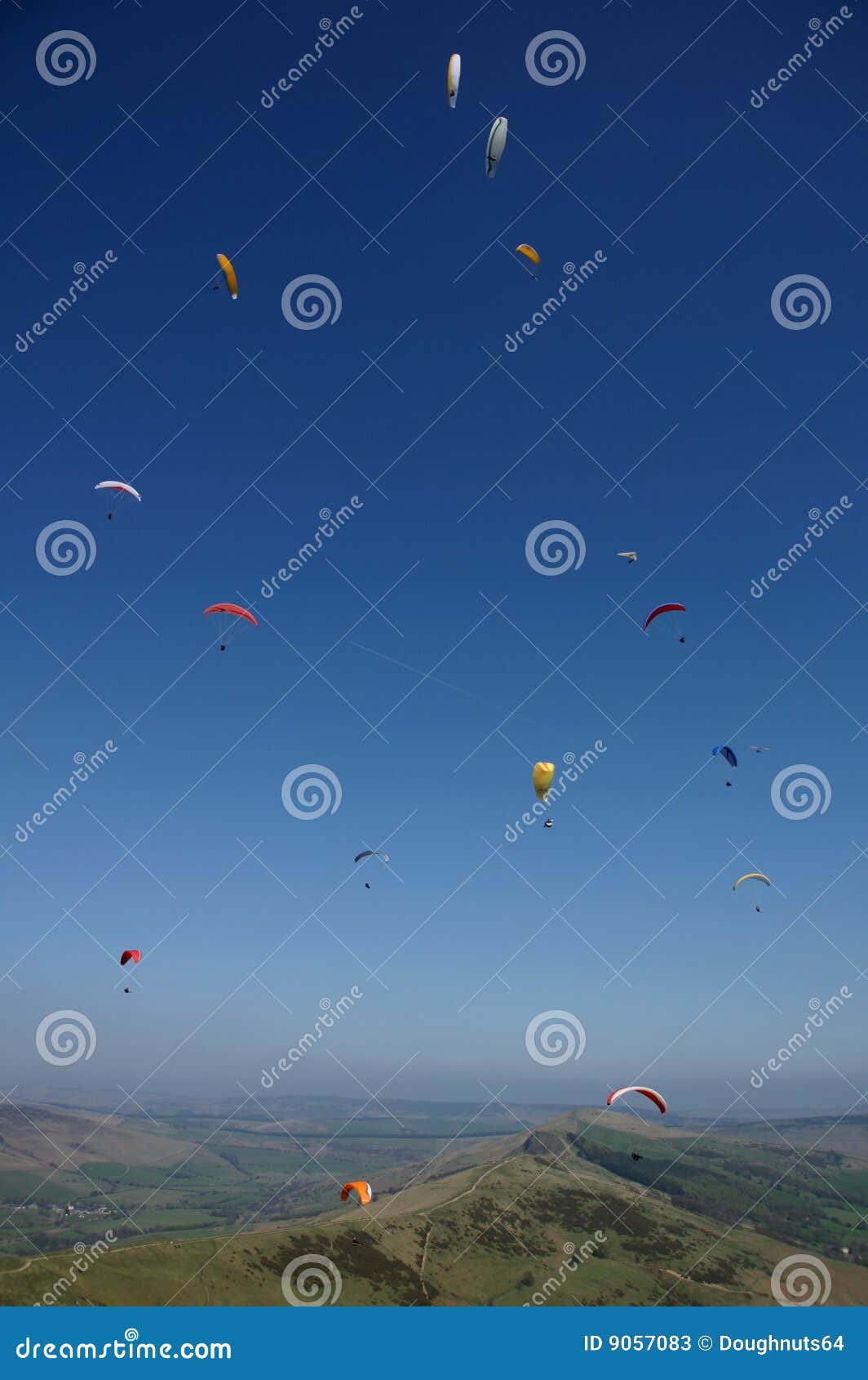 many para-gliders over a green landscape