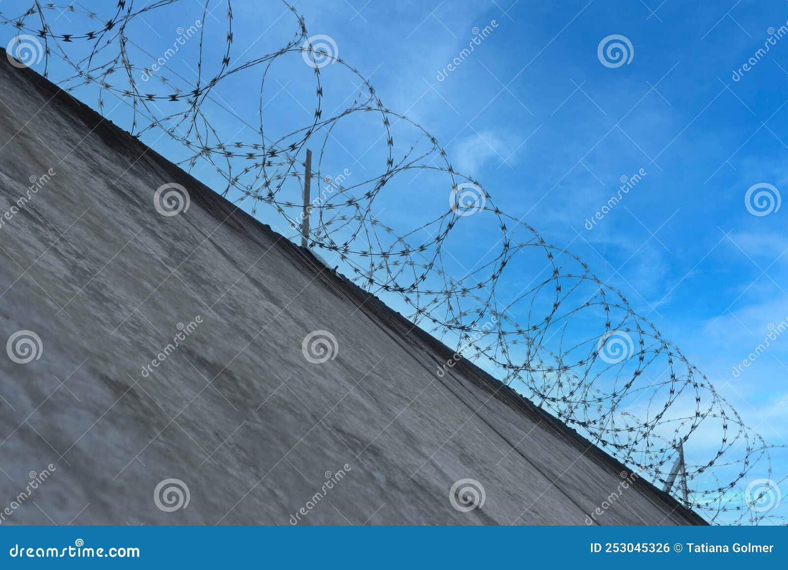 many rows of barbedwire, high concrete fence, barbed wire fence on top, building for execution of punishments for criminals,