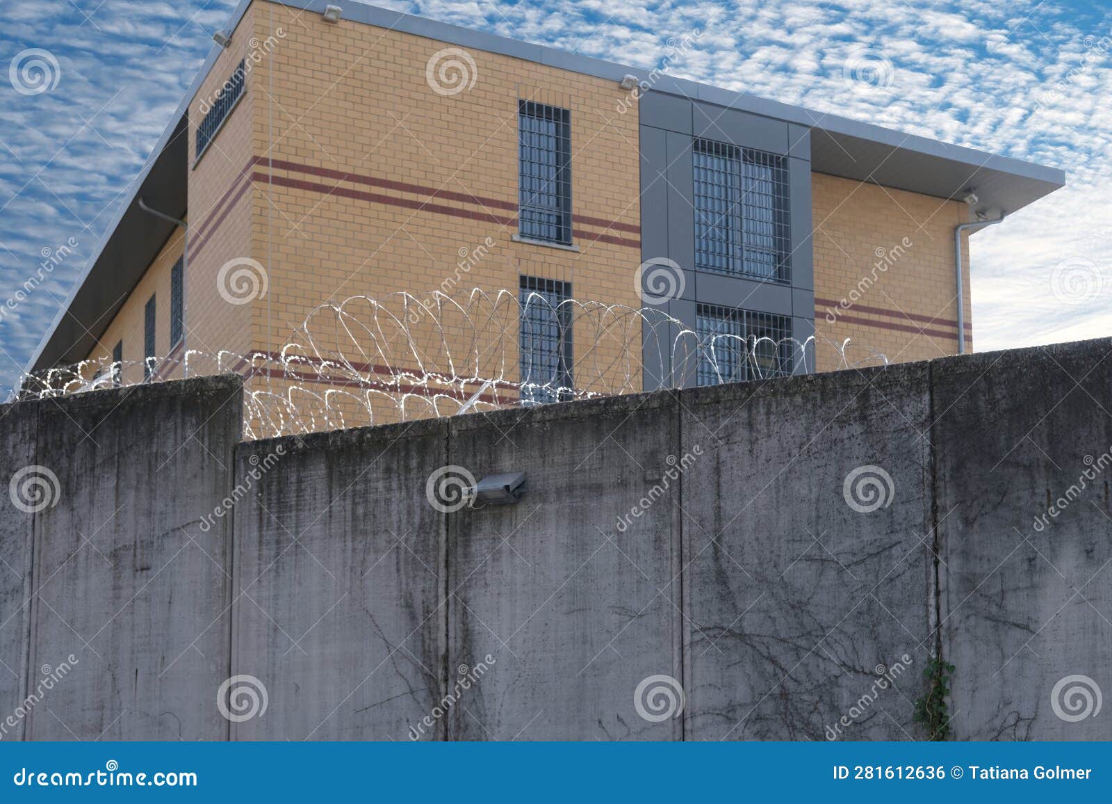 many rows of barbedwire, high concrete fence, barbed wire fence on top, building for execution of punishments for criminals,