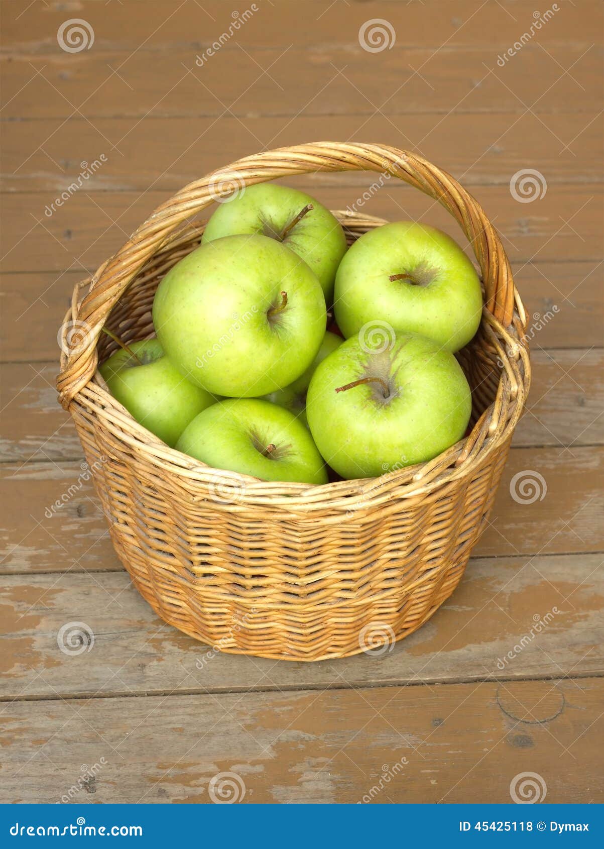 Manzanas verdes maduras en primer de la cesta de mimbre. Todavía vida con las manzanas verdes en cesta de mimbre en el primer del fondo de la madera