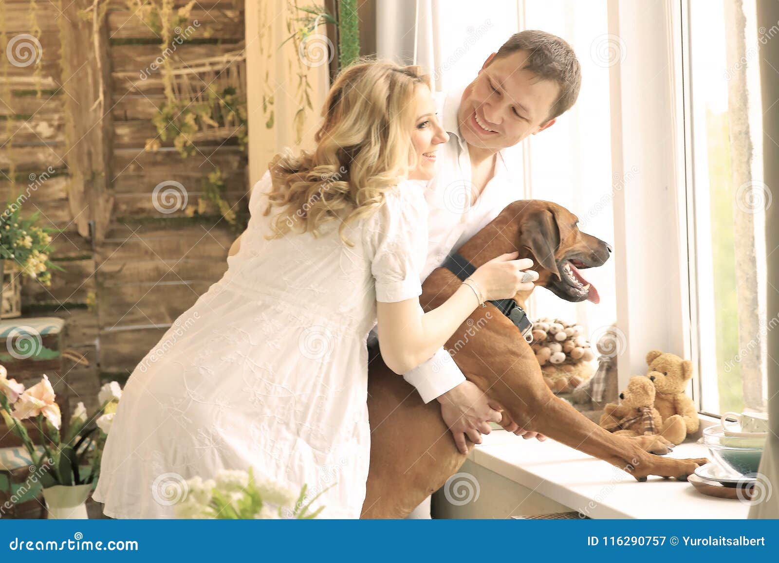 Marito, moglie incinta e un cane che esamina una grande finestra