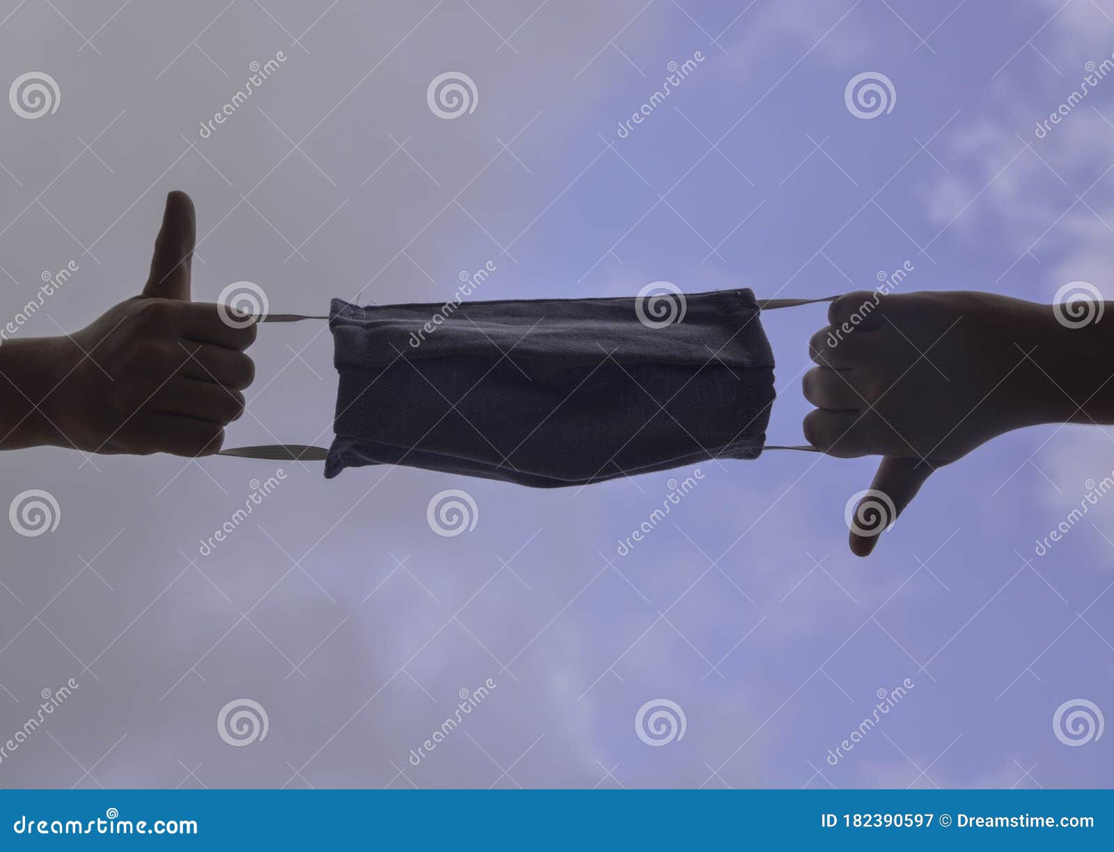 mask pulled by both ends of two hands with thumbs up and down. the background is a cloudy sky. stay home to prevent the quarantine