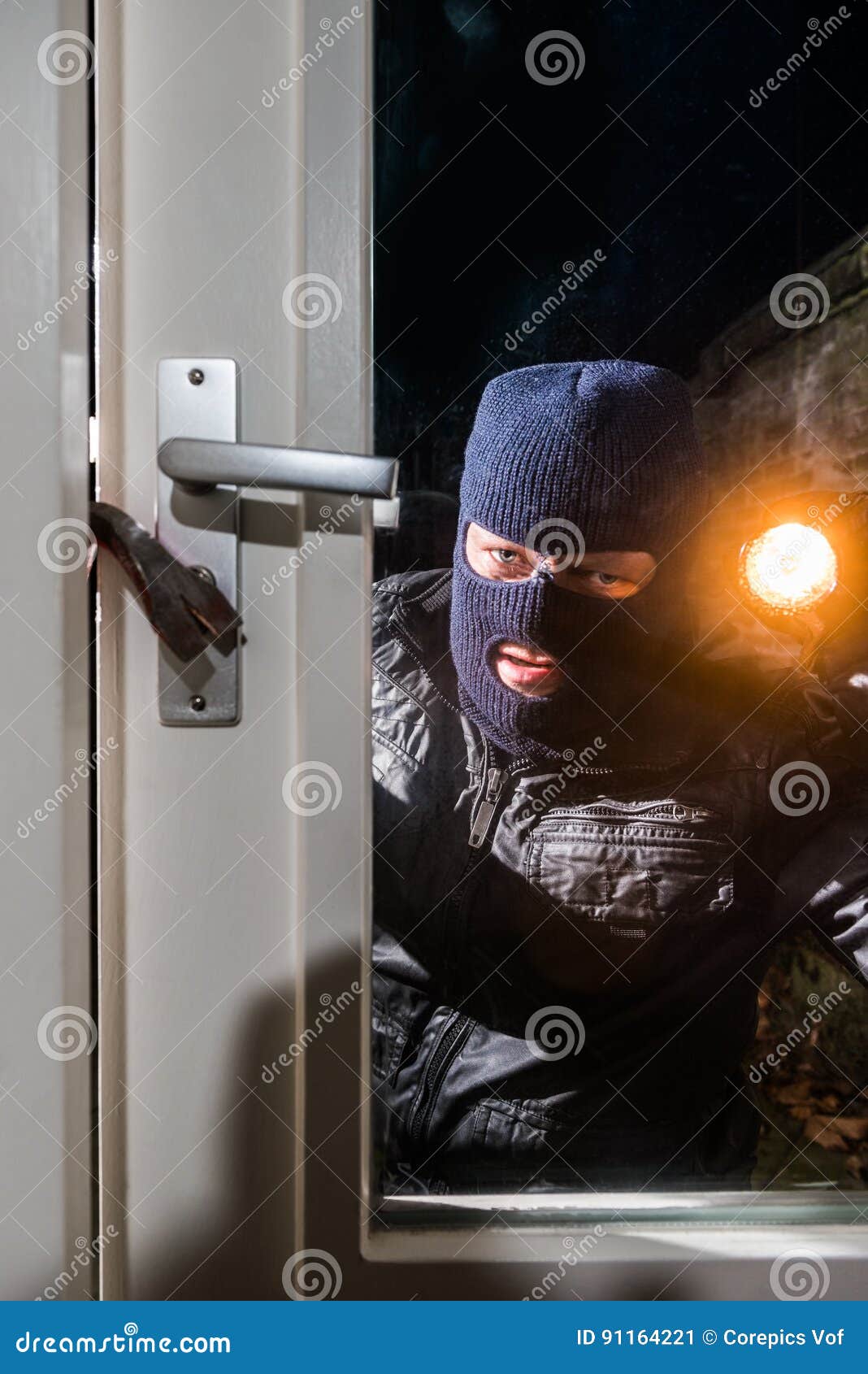 masked intruder holding torch while trying to open window with c
