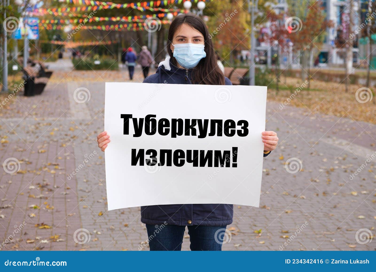 a masked woman holds a poster with text in russian, translated from russian - tuberculosis is curable