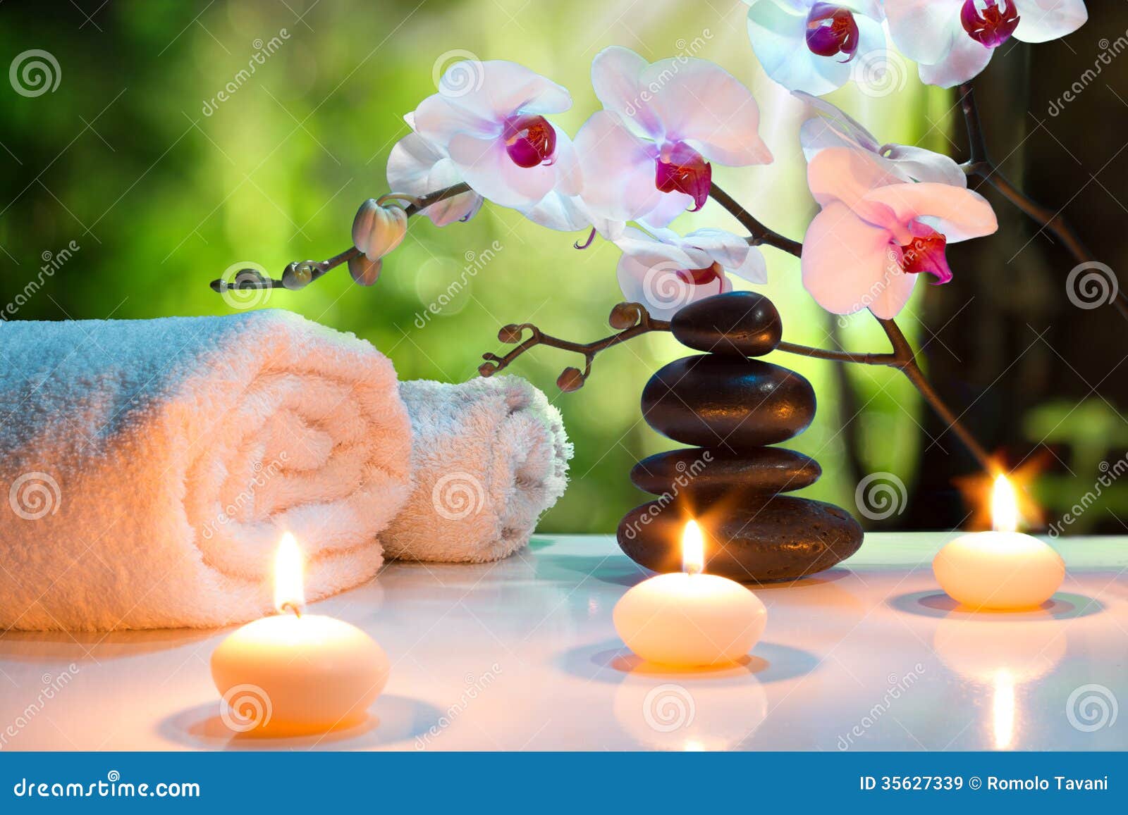 massage composition spa with candles, orchids and black stones in garden