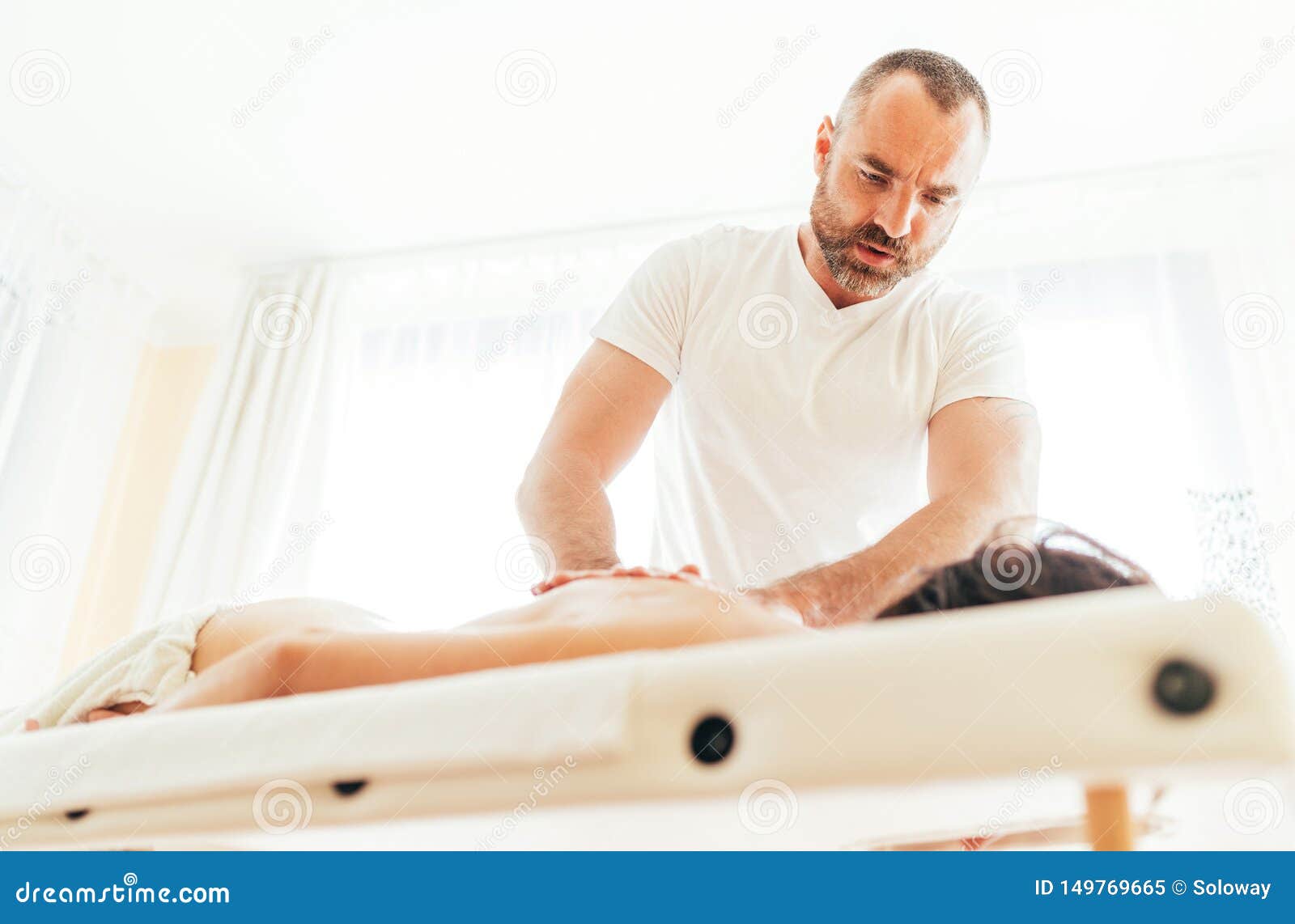 Masseur Man Doing Massage Manipulations On The Client Back And Communicate With Patient Stock