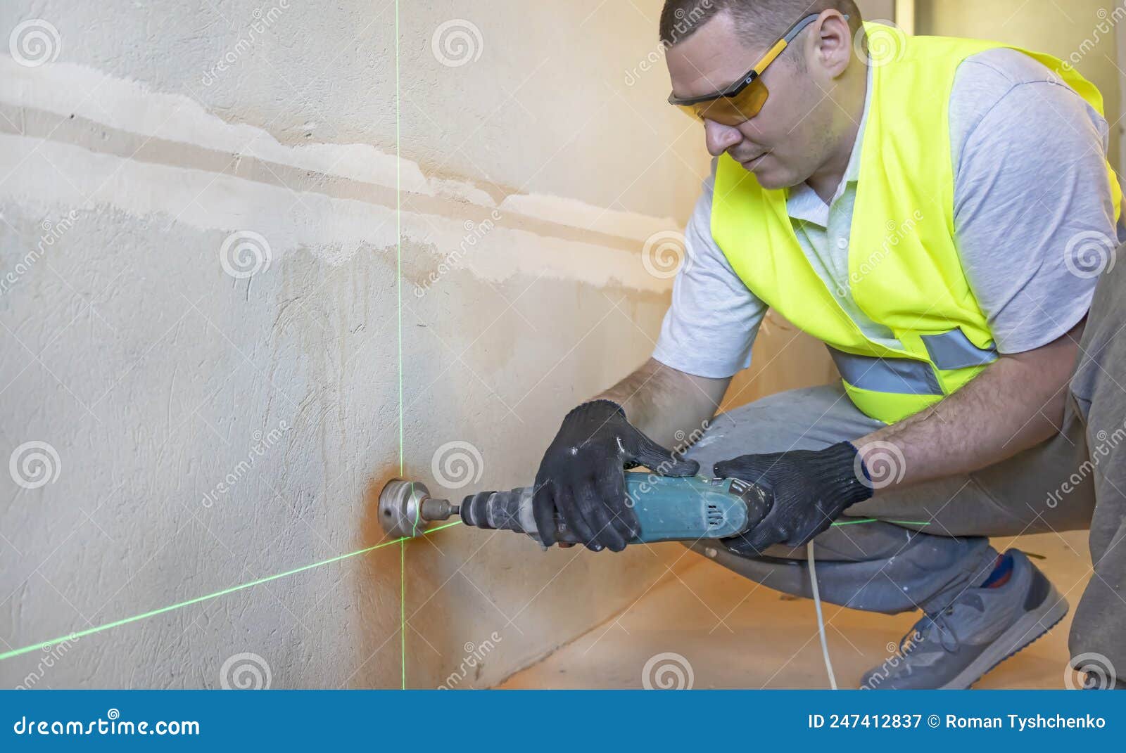 A Master Electrician in Goggles Drills a Hole in the Wall To Install an