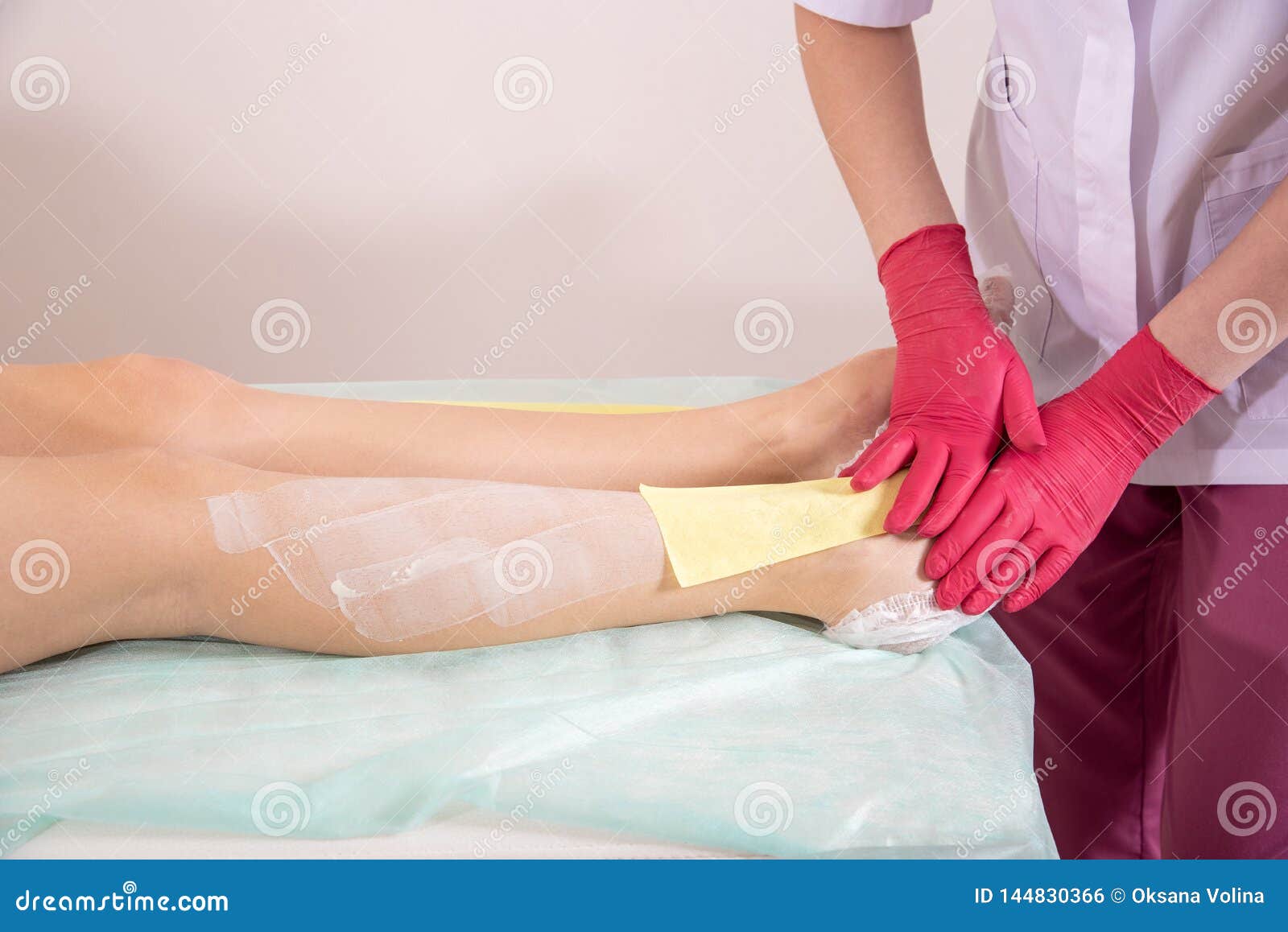 Master In Gloves Makes The Procedure Of Waxing Female Legs Stock Photo