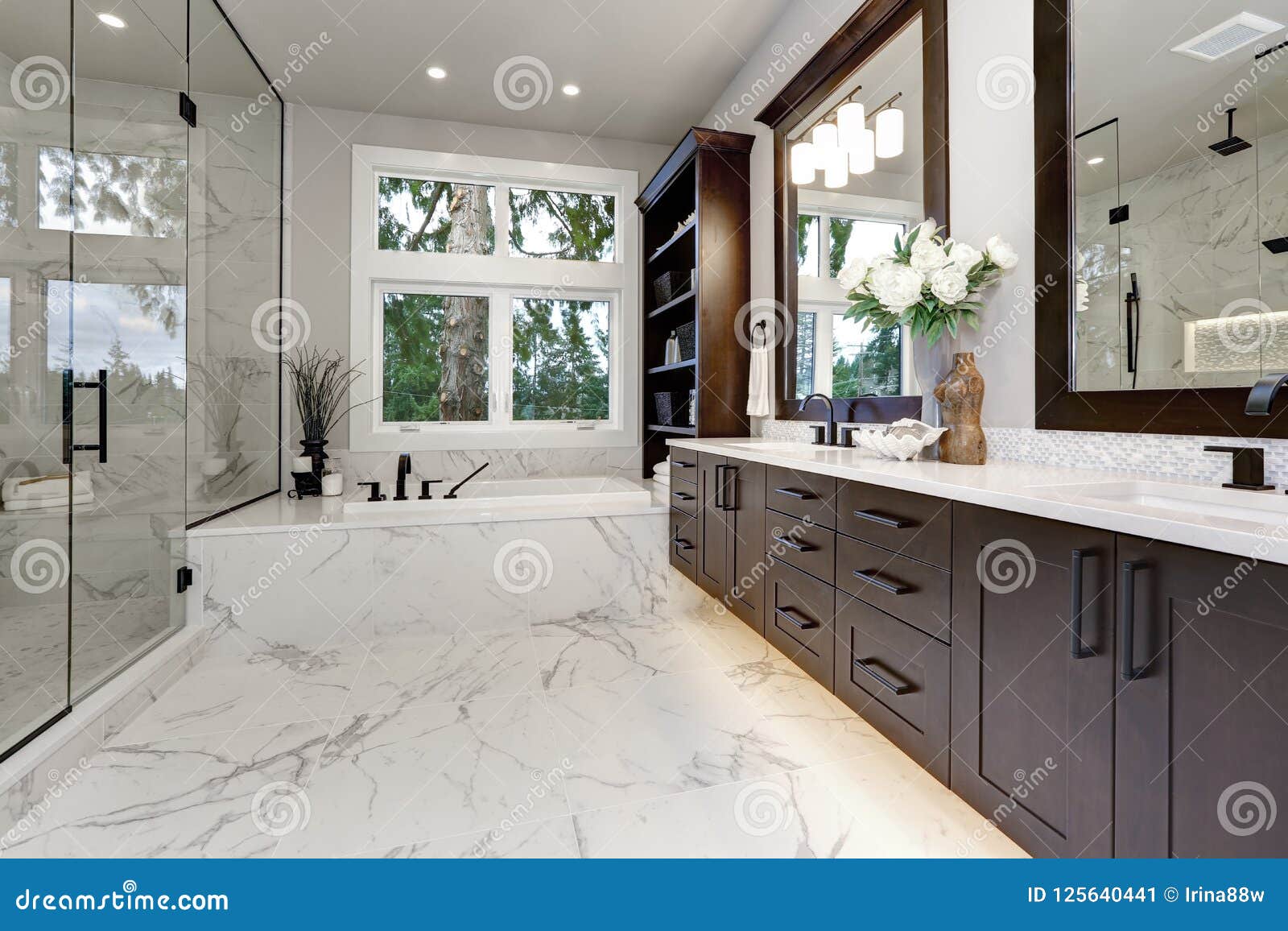 master modern bathroom interior in luxury home with dark hardwood cabinets, white tub and glass door shower