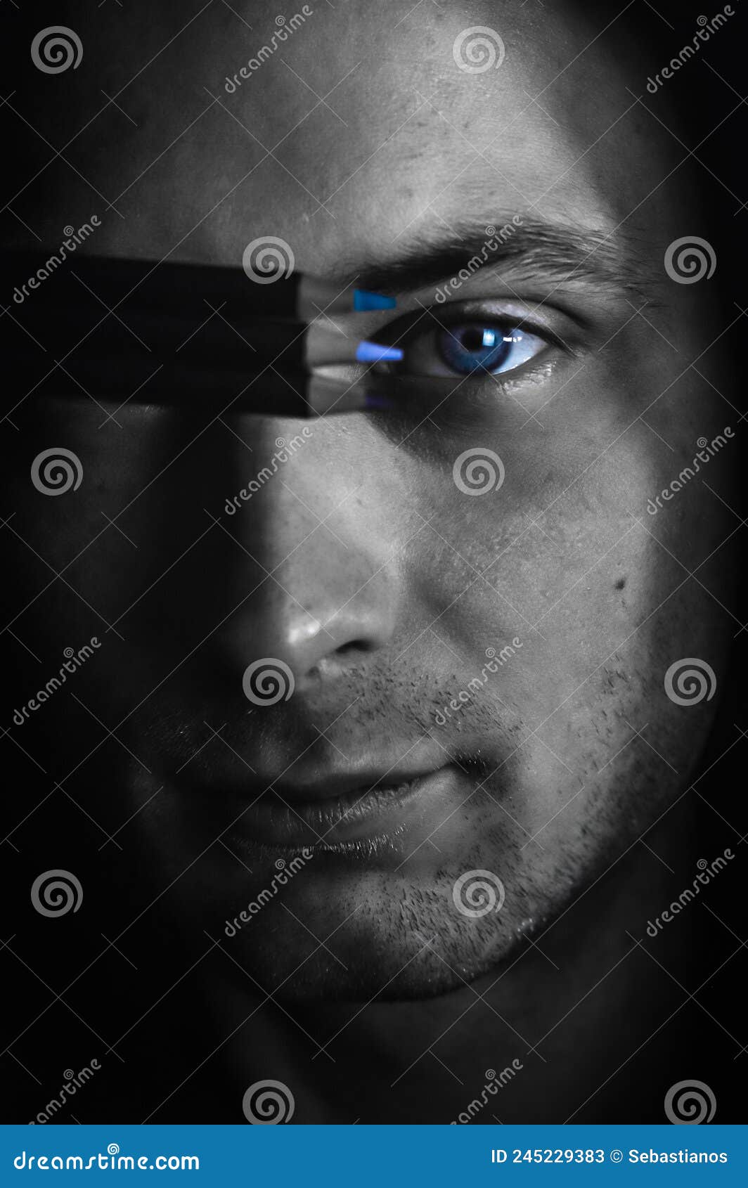 matching colors - black and white portrait of a young blue-eyed man holding three colored pencils near his eye to find the right s