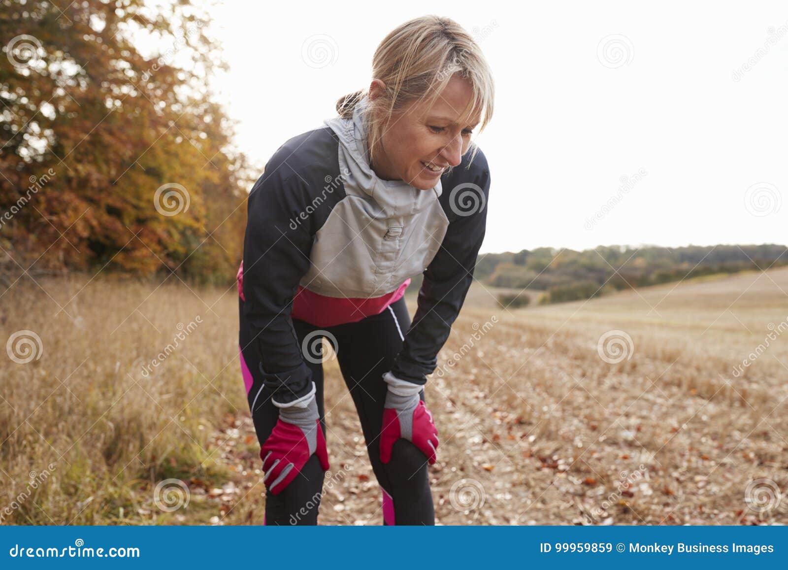 mature female runner pausing for breath during exercise in woods