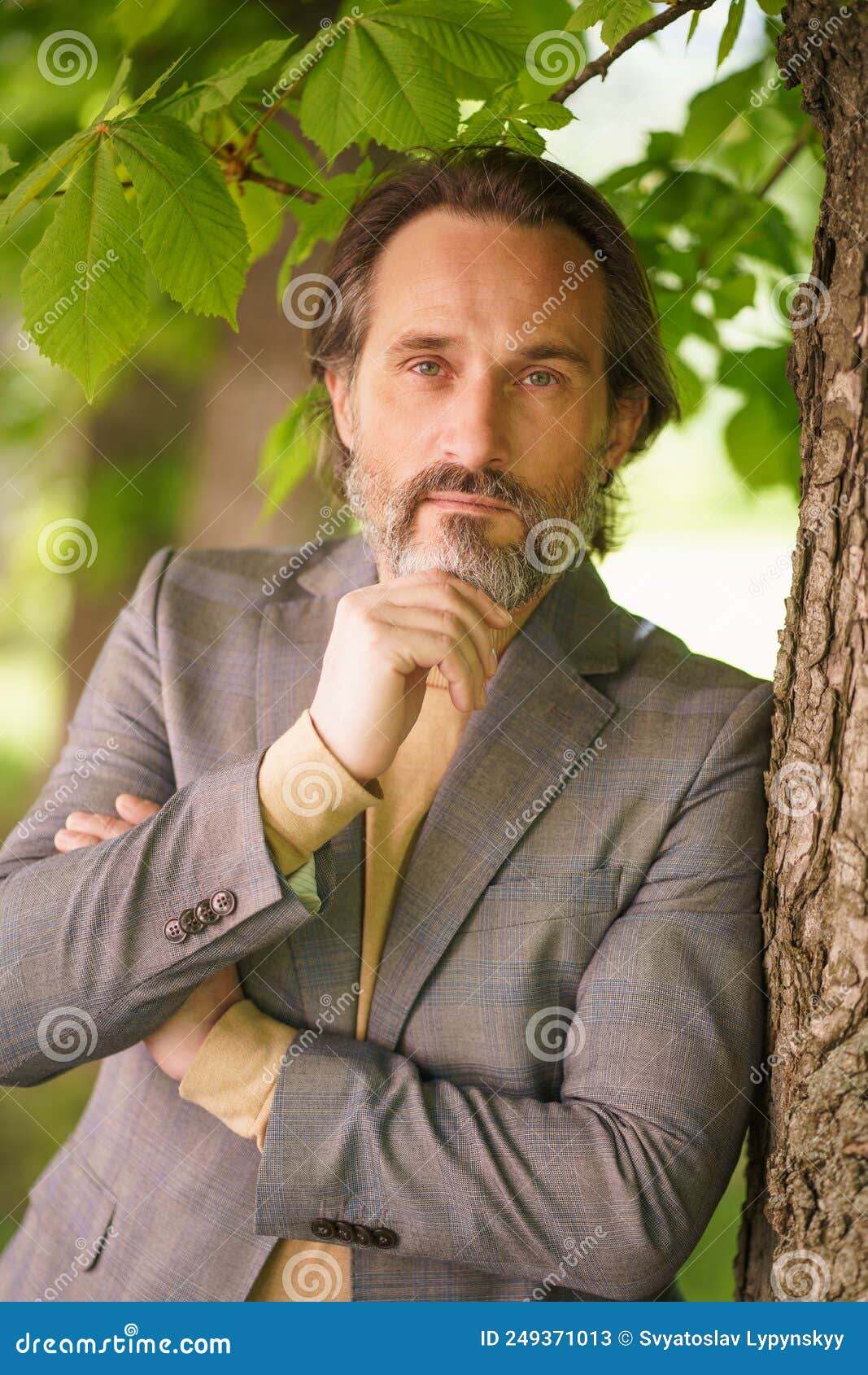Mature Handsome Grey Birded Businessman In Casual Standing Under Tree On The Grass Looking At