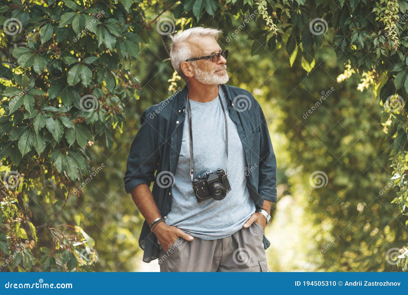 a mature man with a beard walks in the park with a camera. active pastime in old age