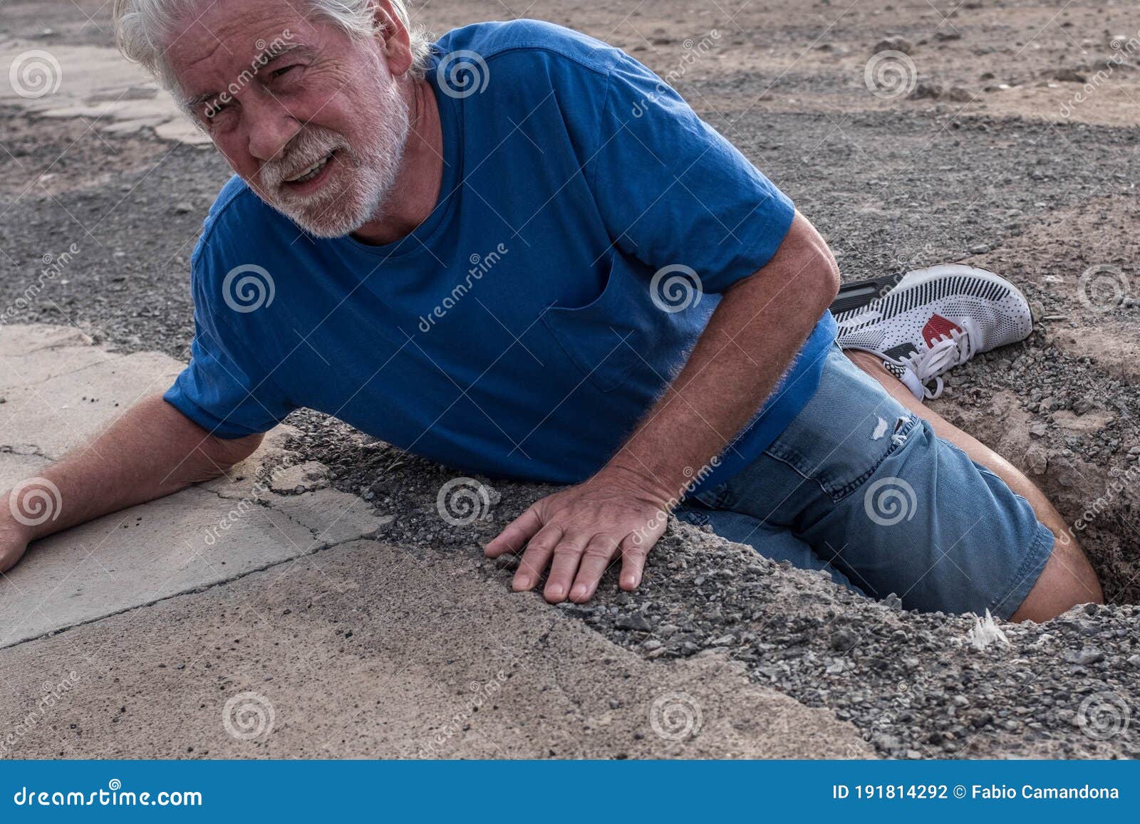 mature man or senior walking in a building zone and falling in a big hole with her leg inside it - needing help on the ground with
