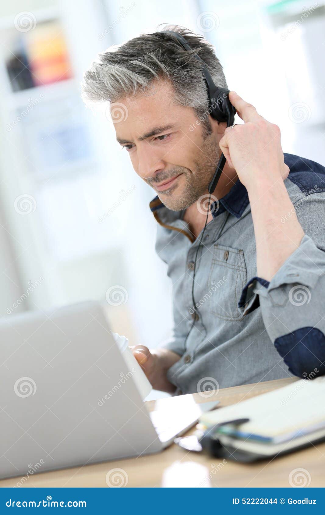 mature man teleworking on laptop using headphones