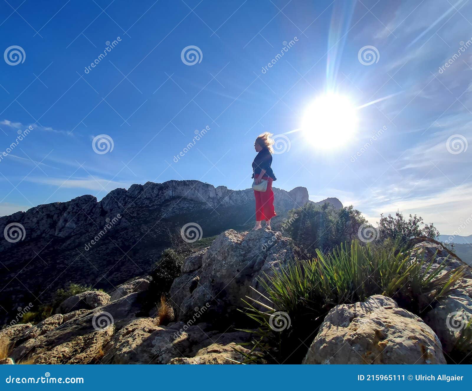mature redhead woman backlight with wind-blown hair on the mountain cim penya roja, els poblets, alicante, spain