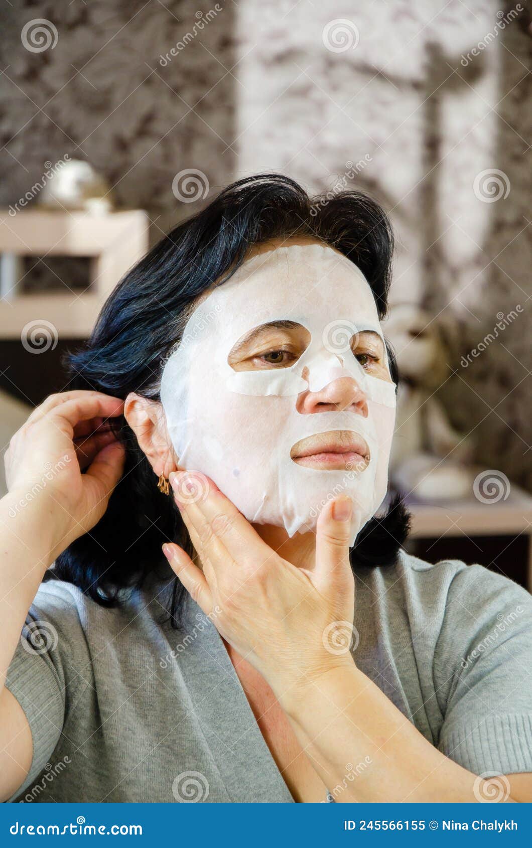 Mature Woman Applies Tissue Cosmetic Mask To Her Face Front Of Mirror Skin Care For Elderly