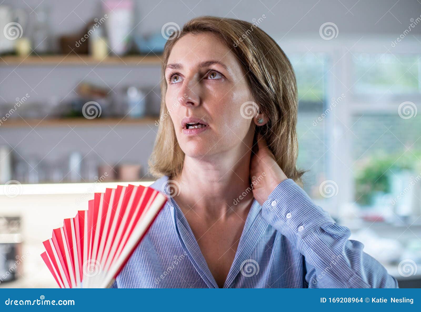 mature woman experiencing hot flush from menopause using fan