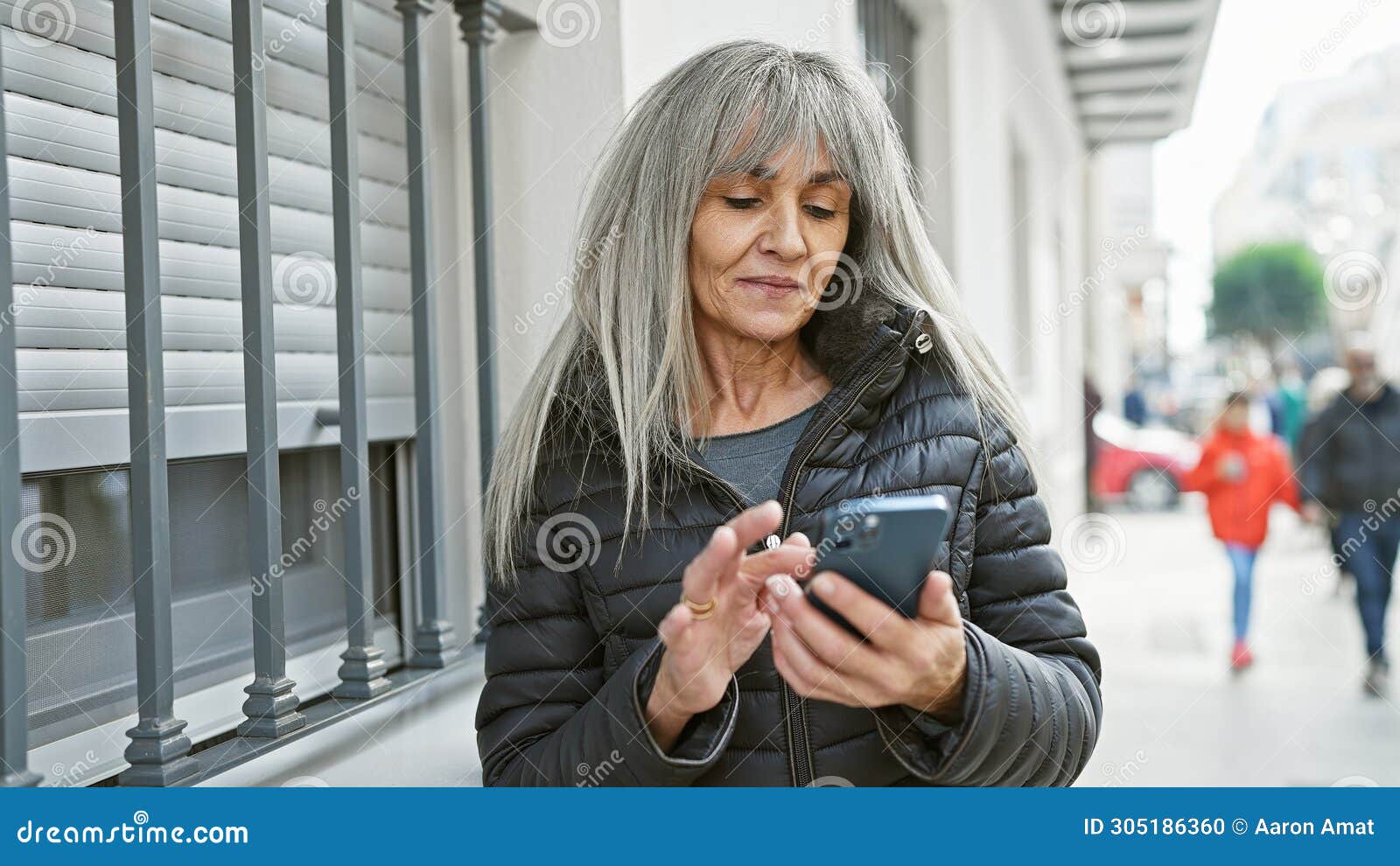 mature woman with grey hair using smartphone on a busy city street