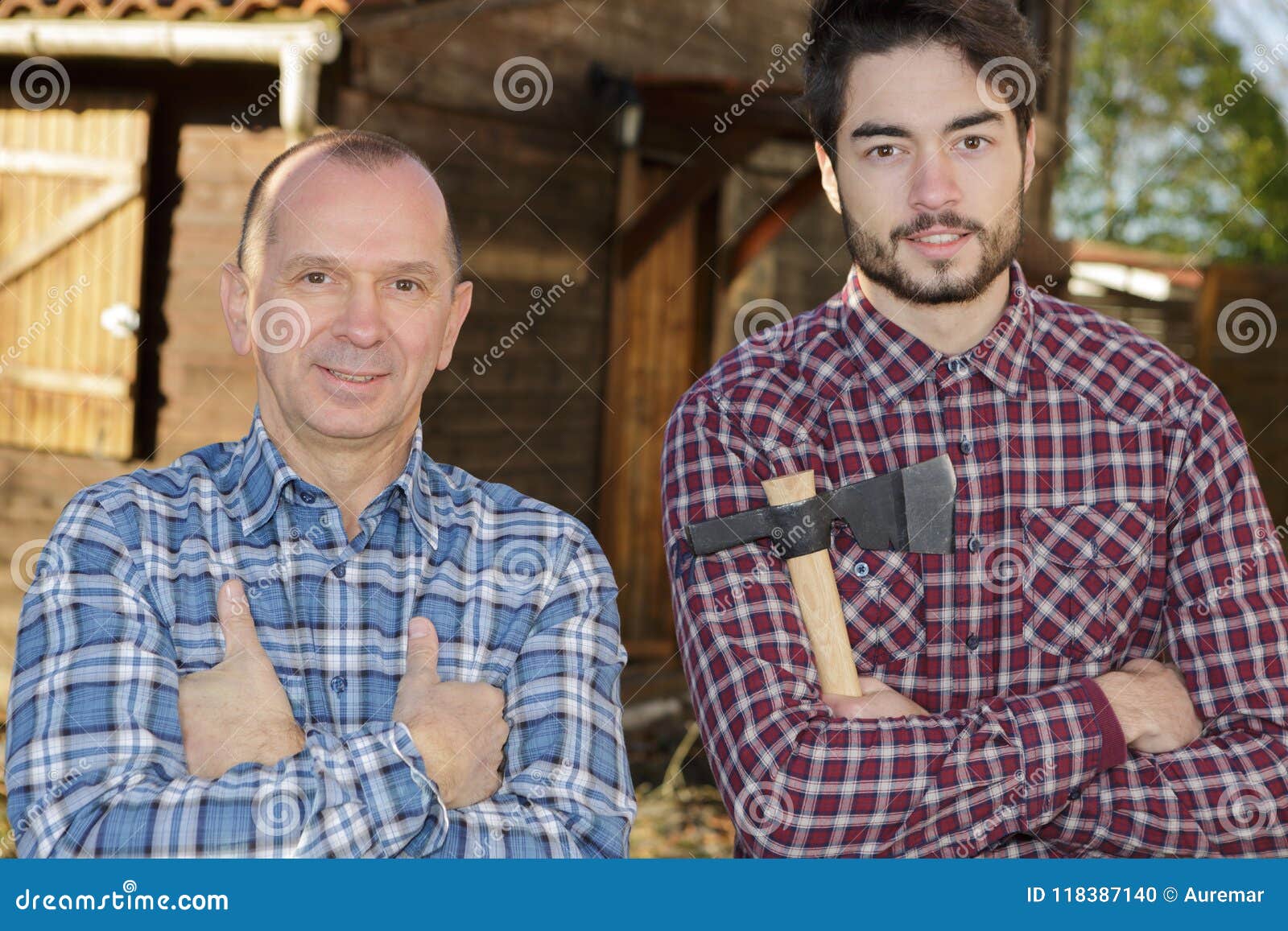 Mature And Young Men Posing Near Wood Hut Holding Axe Stock Photo
