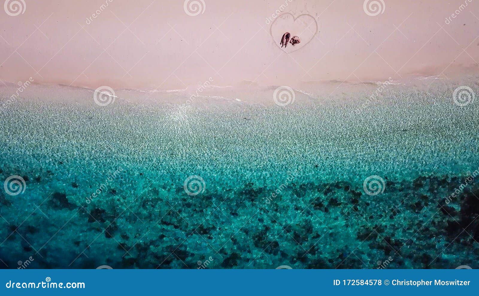 maumere - a drone shot of a couple sitting on a beach in a heart drawn on the sand