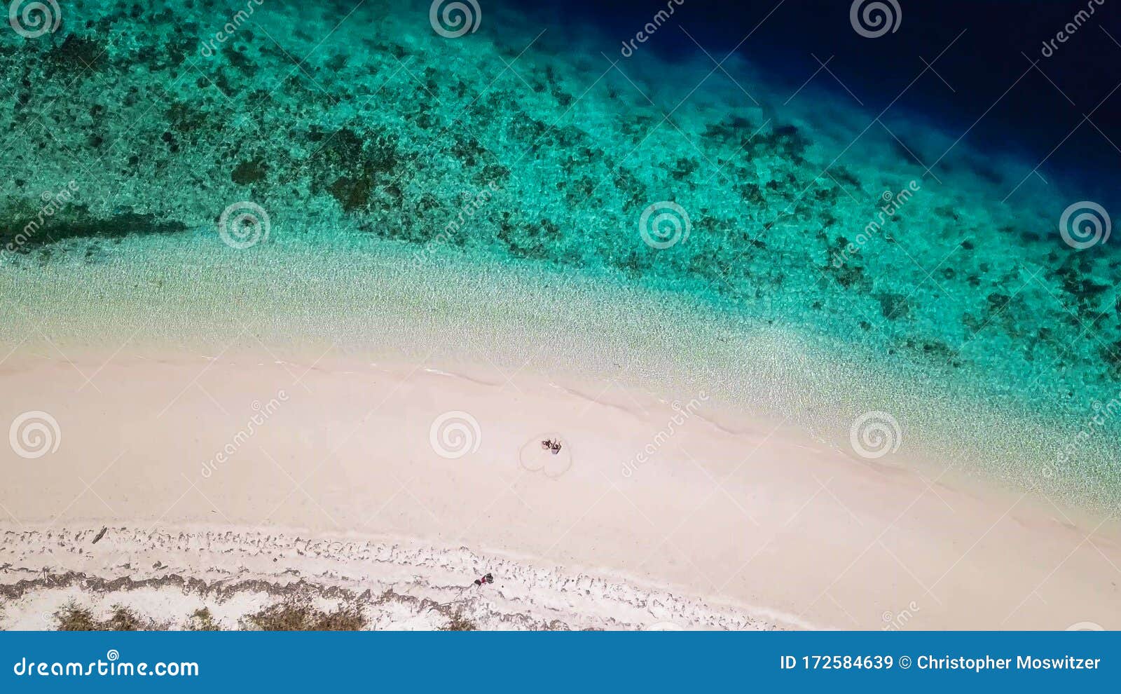 maumere - a drone shot of a couple sitting on a white sand beach