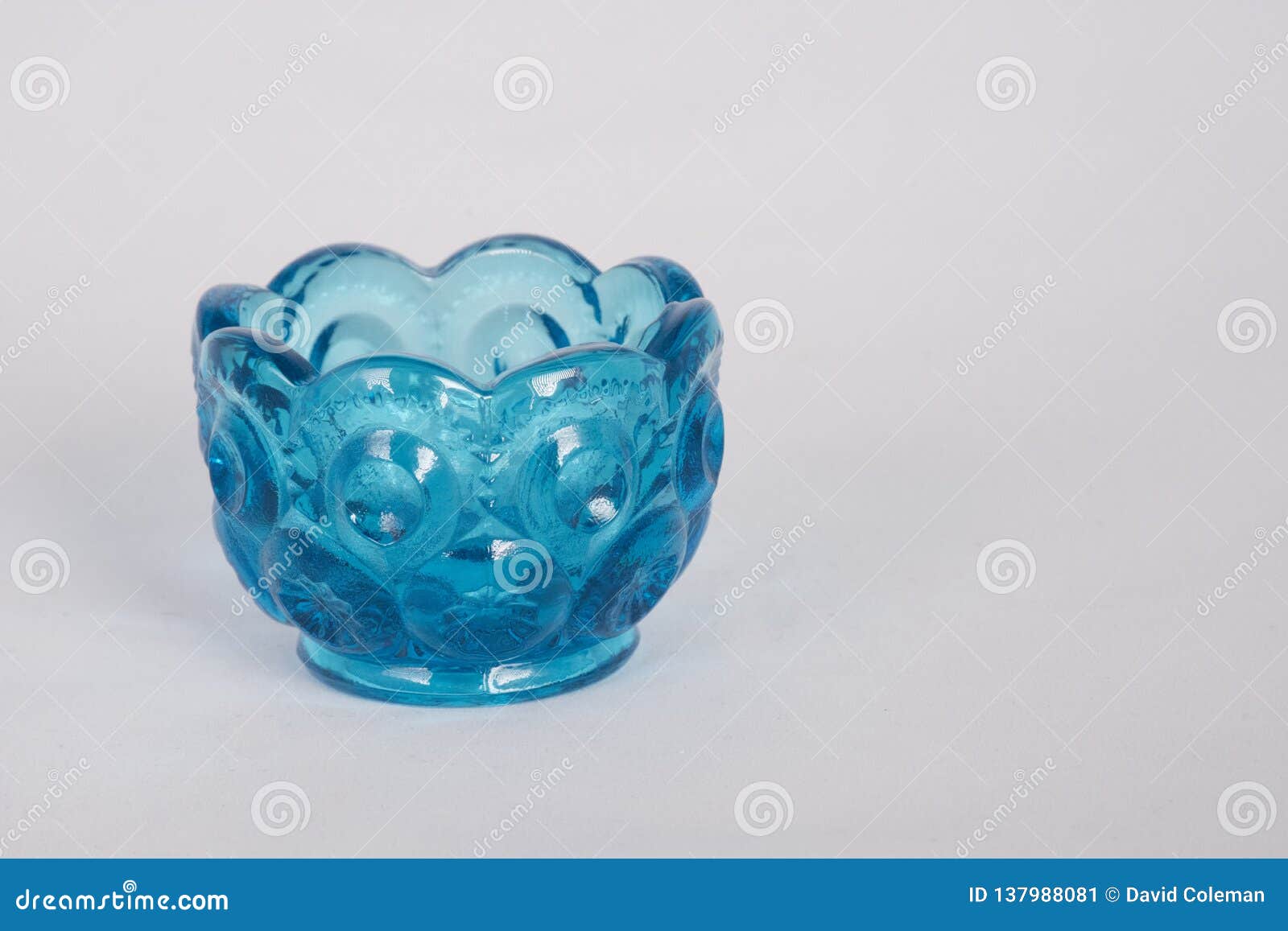 Mały błękitny szklany puchar na bielu. Mały atrakcyjny do kolekcjonowania dekoracyjny szklany puchar z scalloped obręczem i wzorzystym szkłem