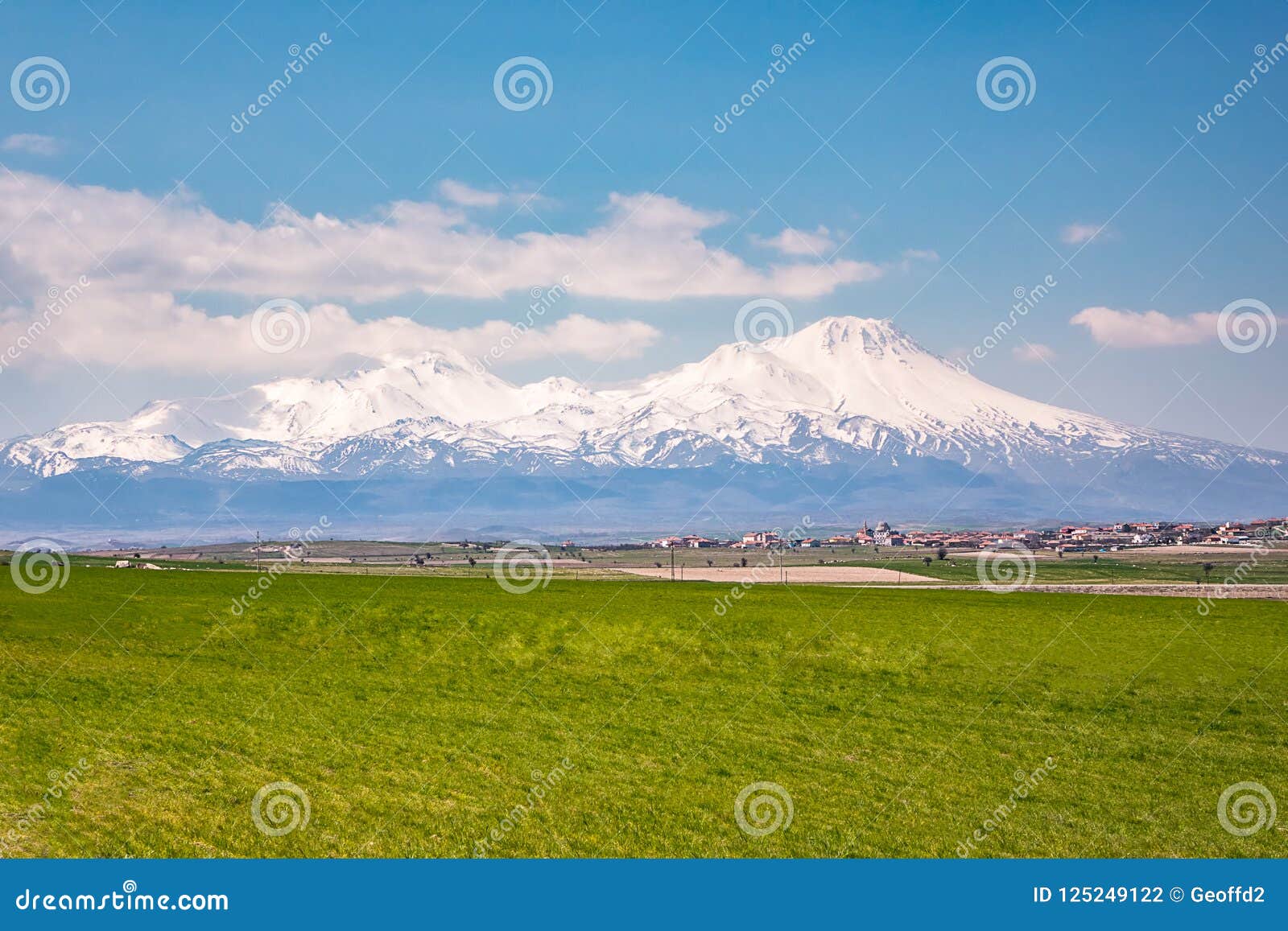 Field Of Grass And Snow Capped Mountains And White Clouds Against A